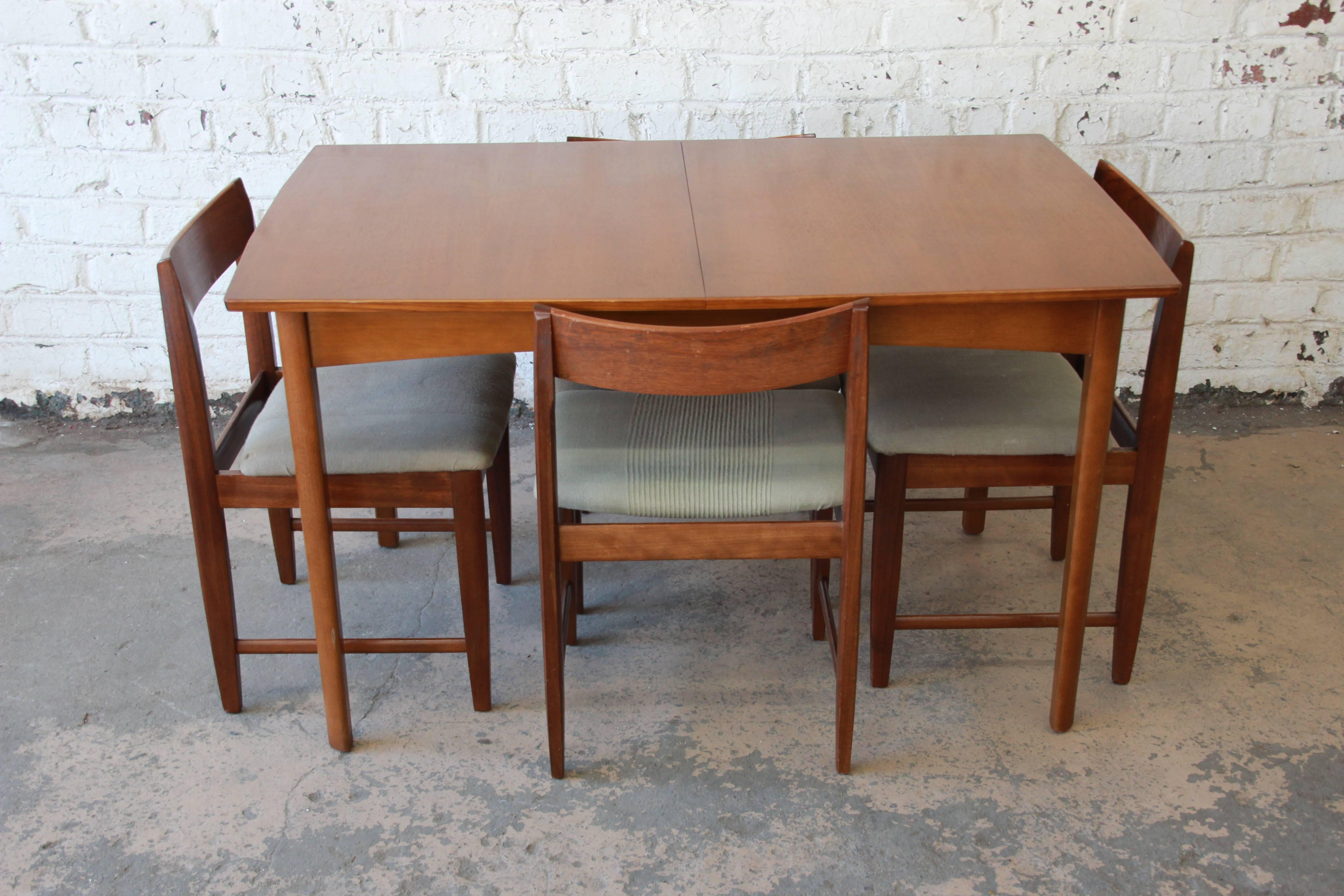 A very nice Mid-Century Modern Danish style teak dining set by G-Plan. The set includes the dining table with a built-in flip-up leaf and four chairs. It features gorgeous teak wood grain and sleek Mid-Century Modern design. The table and chairs are