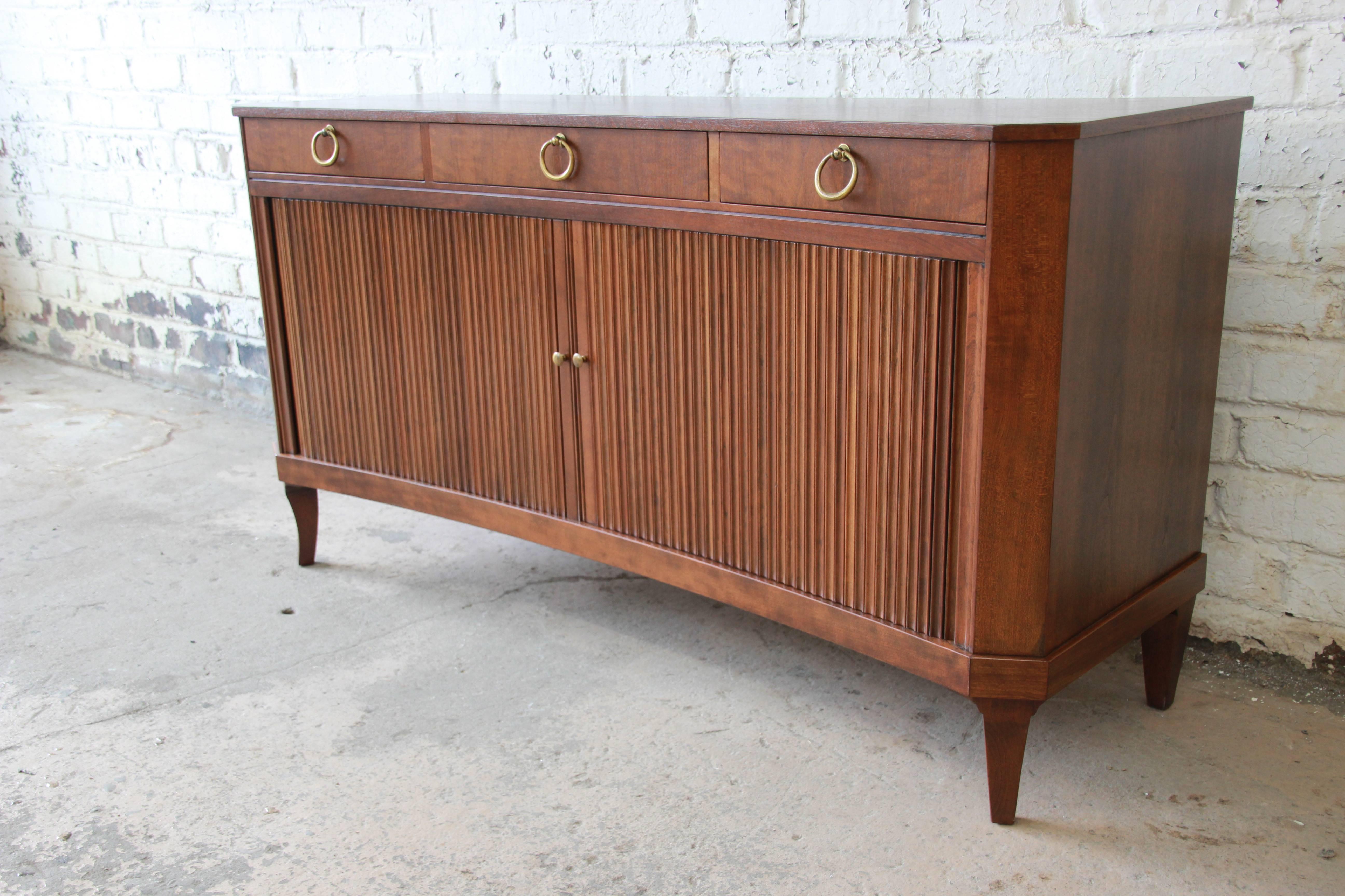 An exceptional midcentury Regency style curved front tambour door sideboard or credenza designed by Michael Taylor for Baker Furniture. The credenza is made from solid fruitwood and features a curved front with canted corners and beautiful tambour