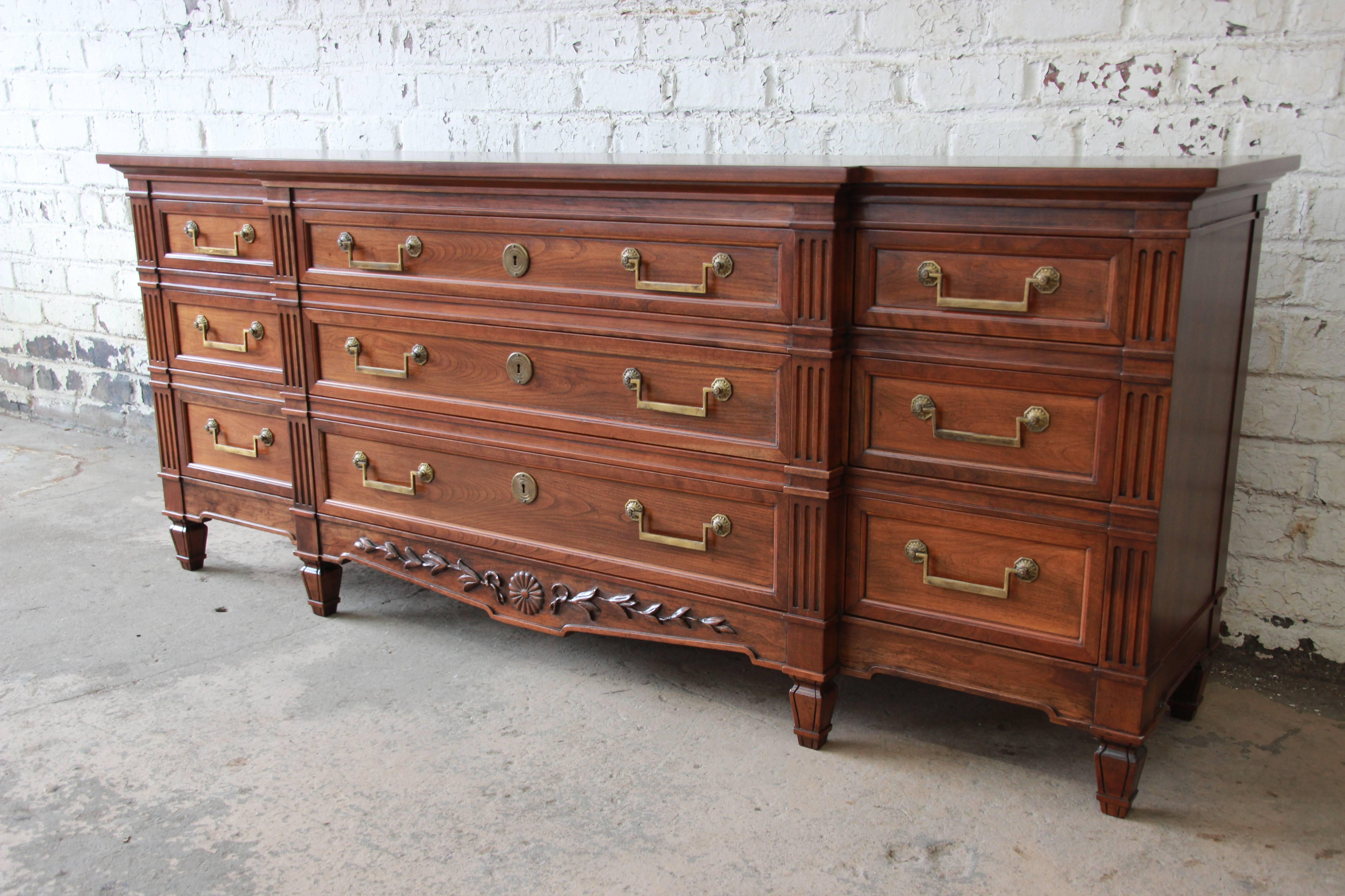 An outstanding vintage French Regency style solid cherrywood triple dresser or credenza by Baker Furniture. The dresser features gorgeous cherrywood grain with beautiful carved wood details. It offers ample room for storage, with nine dovetailed
