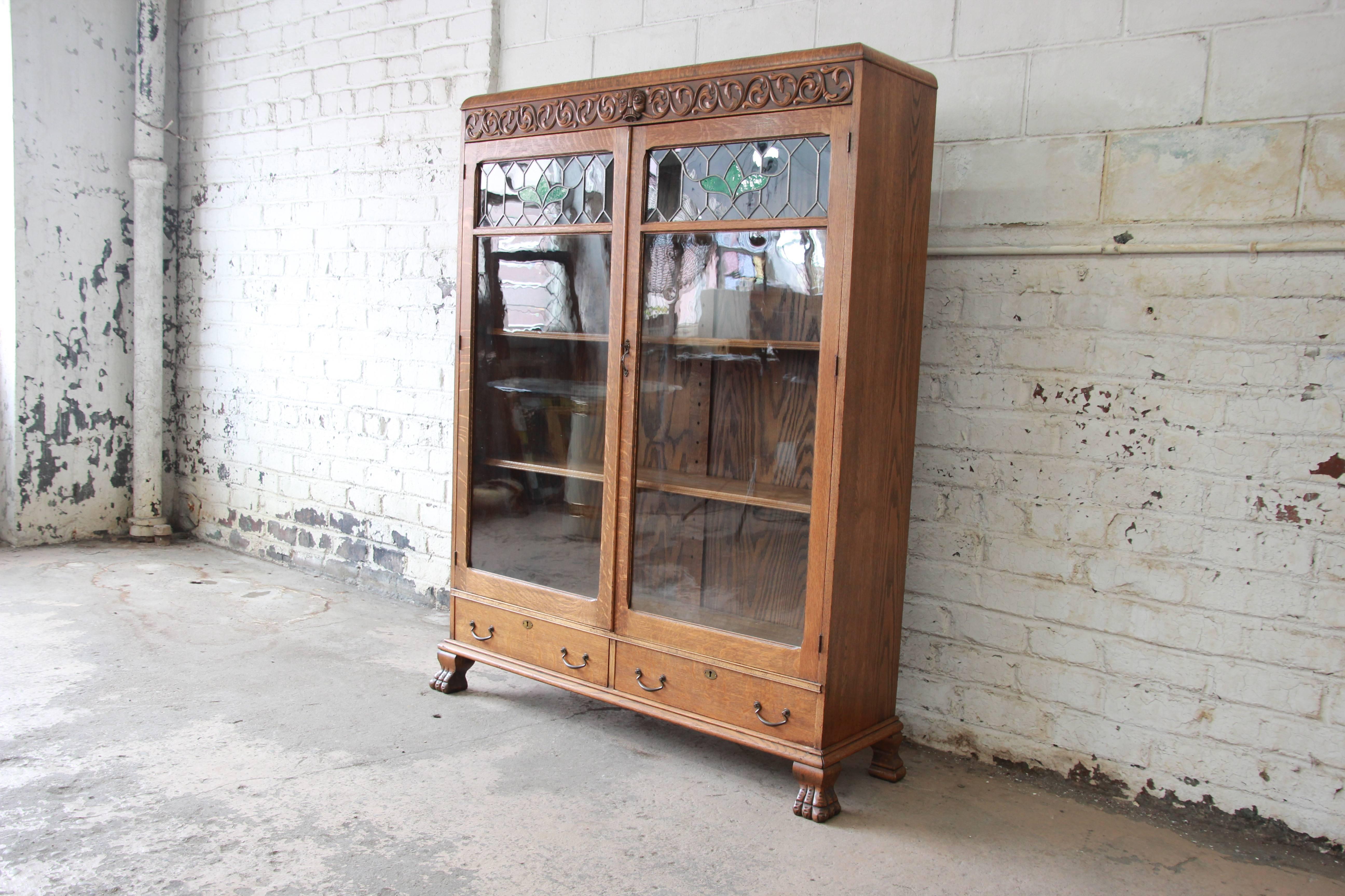 An exceptional antique carved oak bookcase. The bookcase features gorgeous quarter sawn oak wood grain and beautiful leaded stained glass doors. There are nice carved wood details along the top of the bookcase, including a carved face. The case
