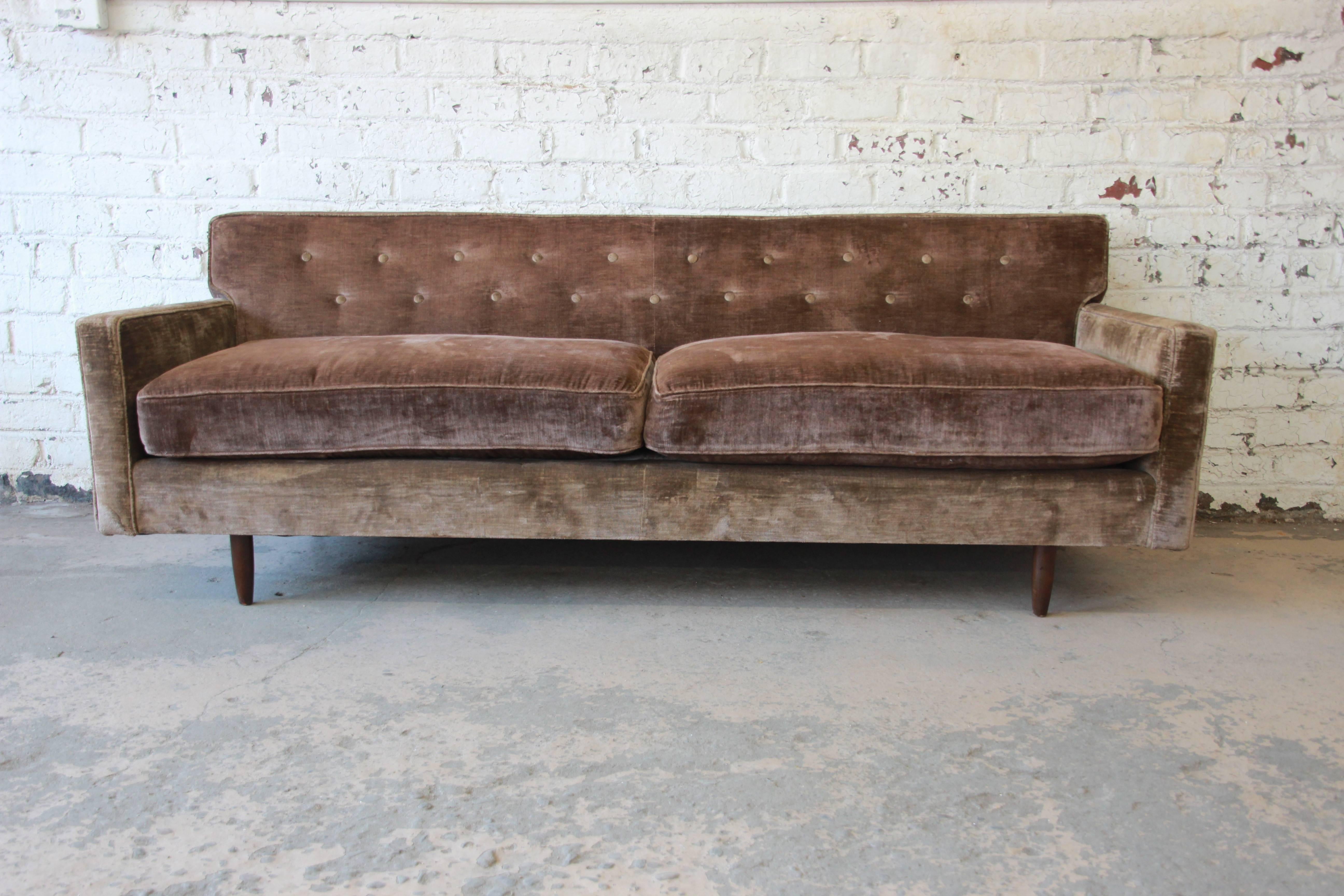 A gorgeous Mid-Century Modern tufted brown velvet sofa by Baker Furniture. The sofa features nice brown velvet upholstery, with a unique herringbone-patterned fabric on the back. It has nice clean midcentury lines and sits on straight solid walnut