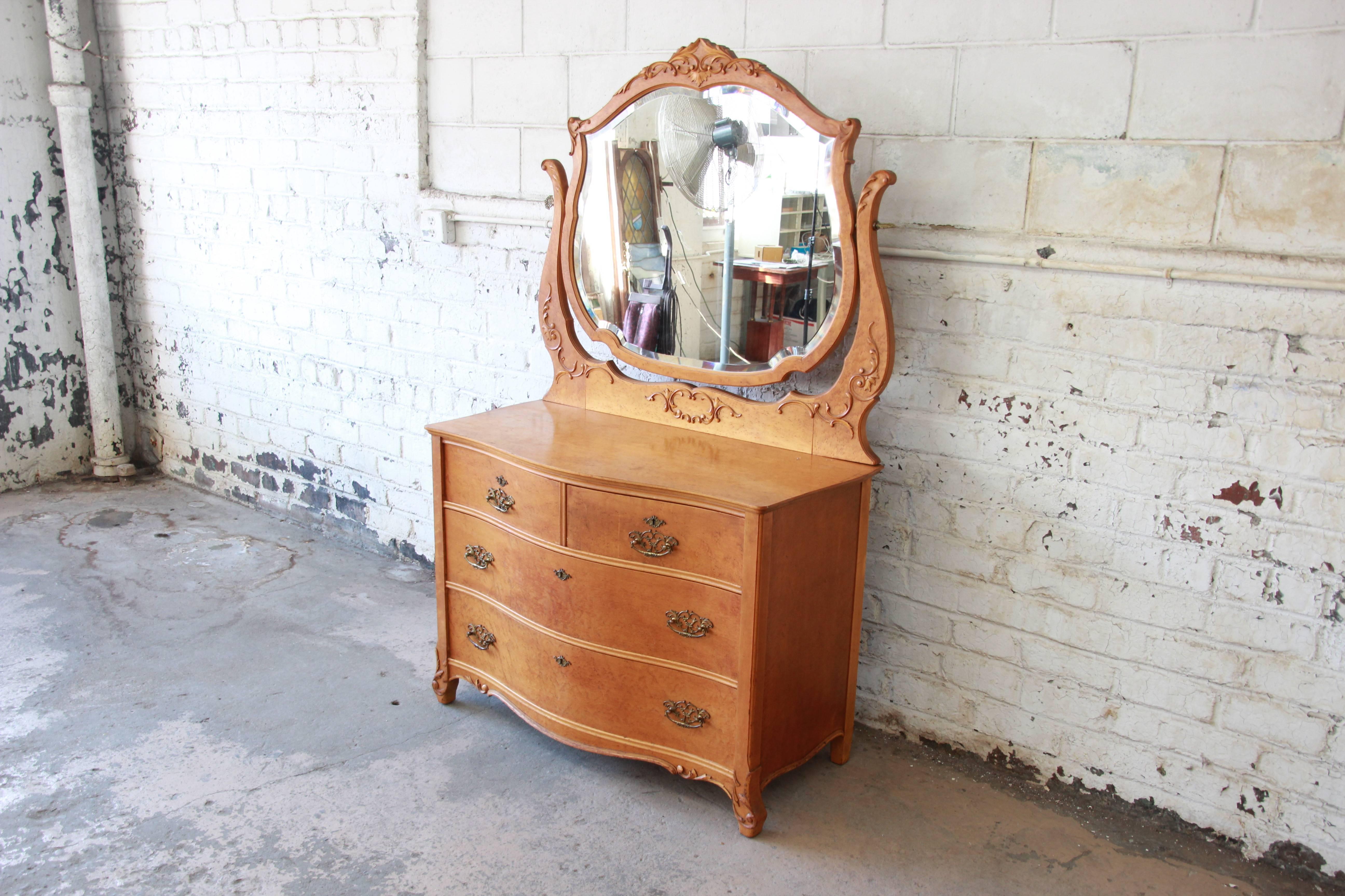 A gorgeous antique bird's-eye maple dresser by Widdicomb Furniture Co. of Grand Rapids. The dresser features beautiful bird's-eye maple wood grain, original brass hardware, and a nicely carved bevelled swing mirror. It offers ample room for storage,