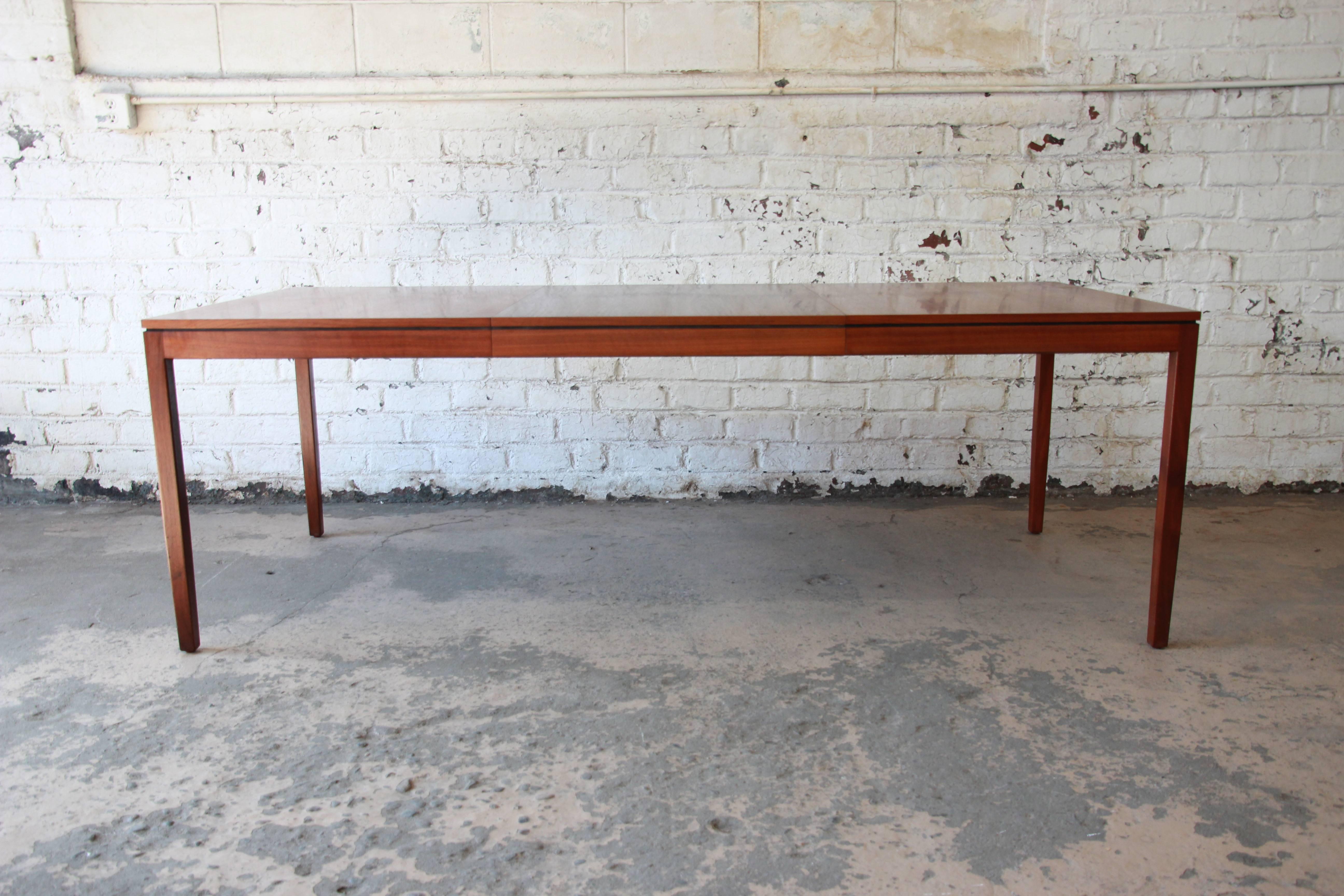A simple, elegant, walnut Mid-Century Modern extension dining table designed by Florence Knoll. Table includes a 28