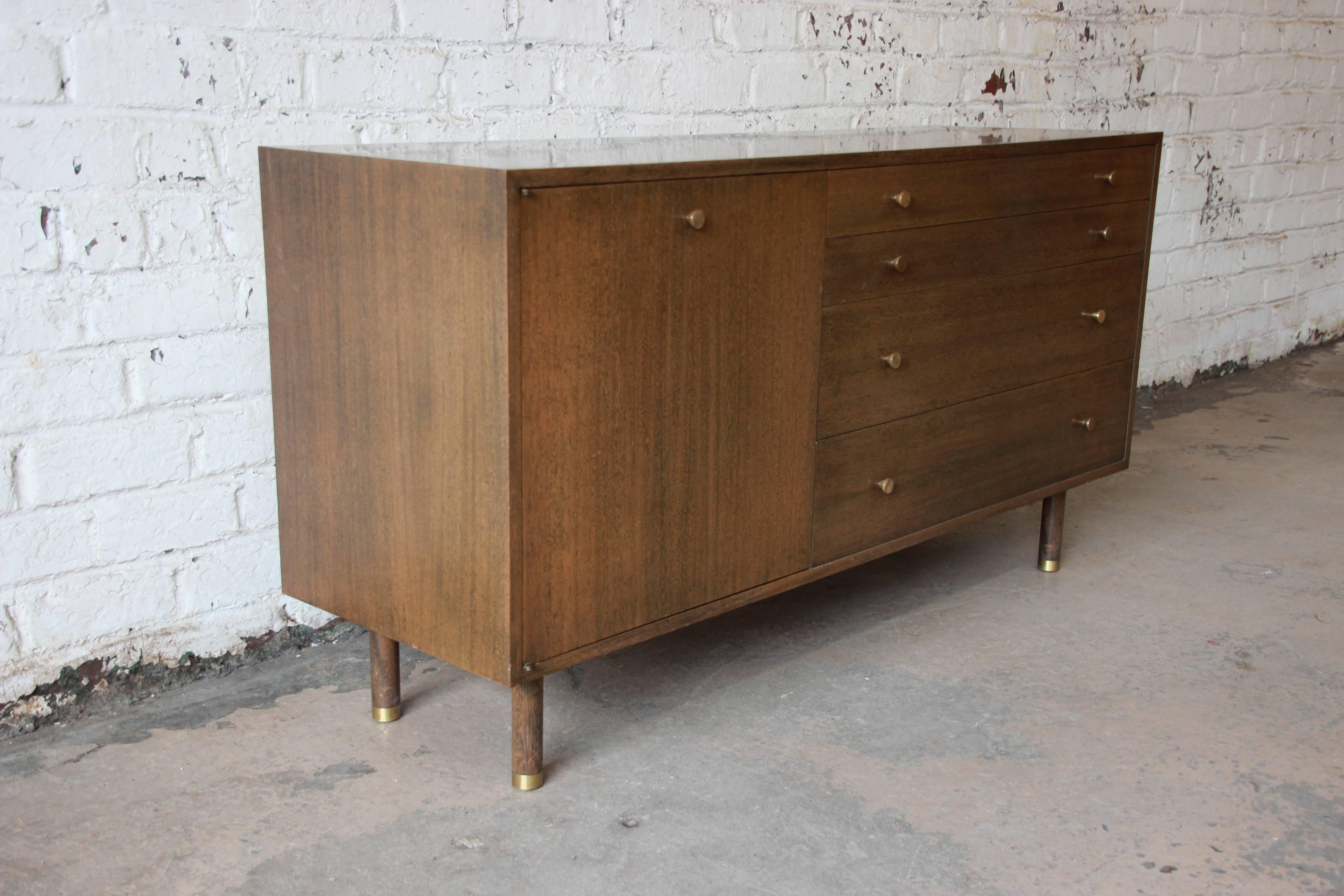 An exceptional Mid-Century Modern credenza designed by Harvey Probber. The credenza features beautiful mahogany wood grain in an ash finish, sleek Mid-Century lines, and original brass hardware. It offers ample room for storage with four drawers and