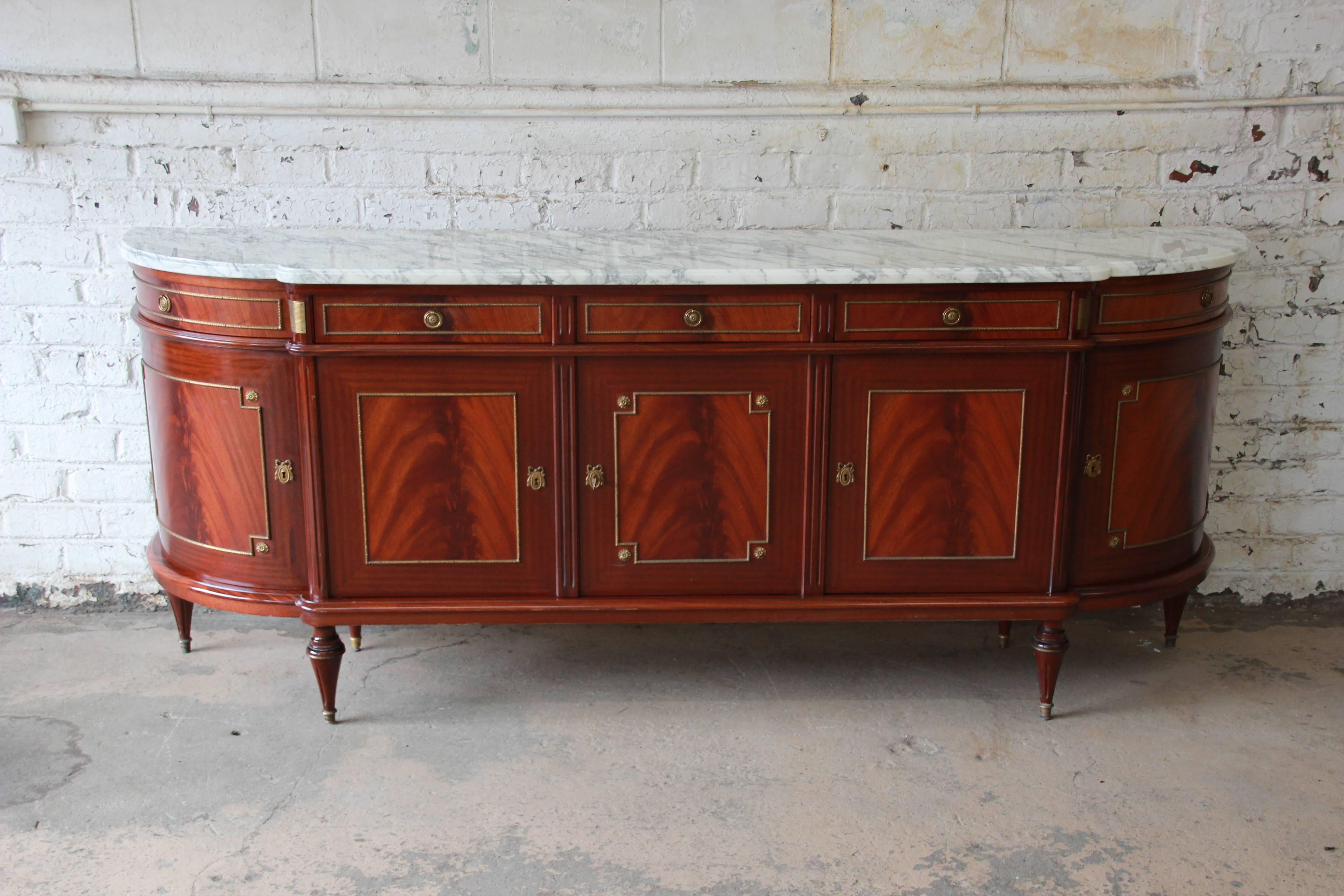 A truly outstanding monumental Maison Jansen marble-top Directoire sideboard or console table in Louis XVI style. This fantastic neoclassical sideboard features stunning flame mahogany wood grain with exquisite bronze-mounted details. It offers
