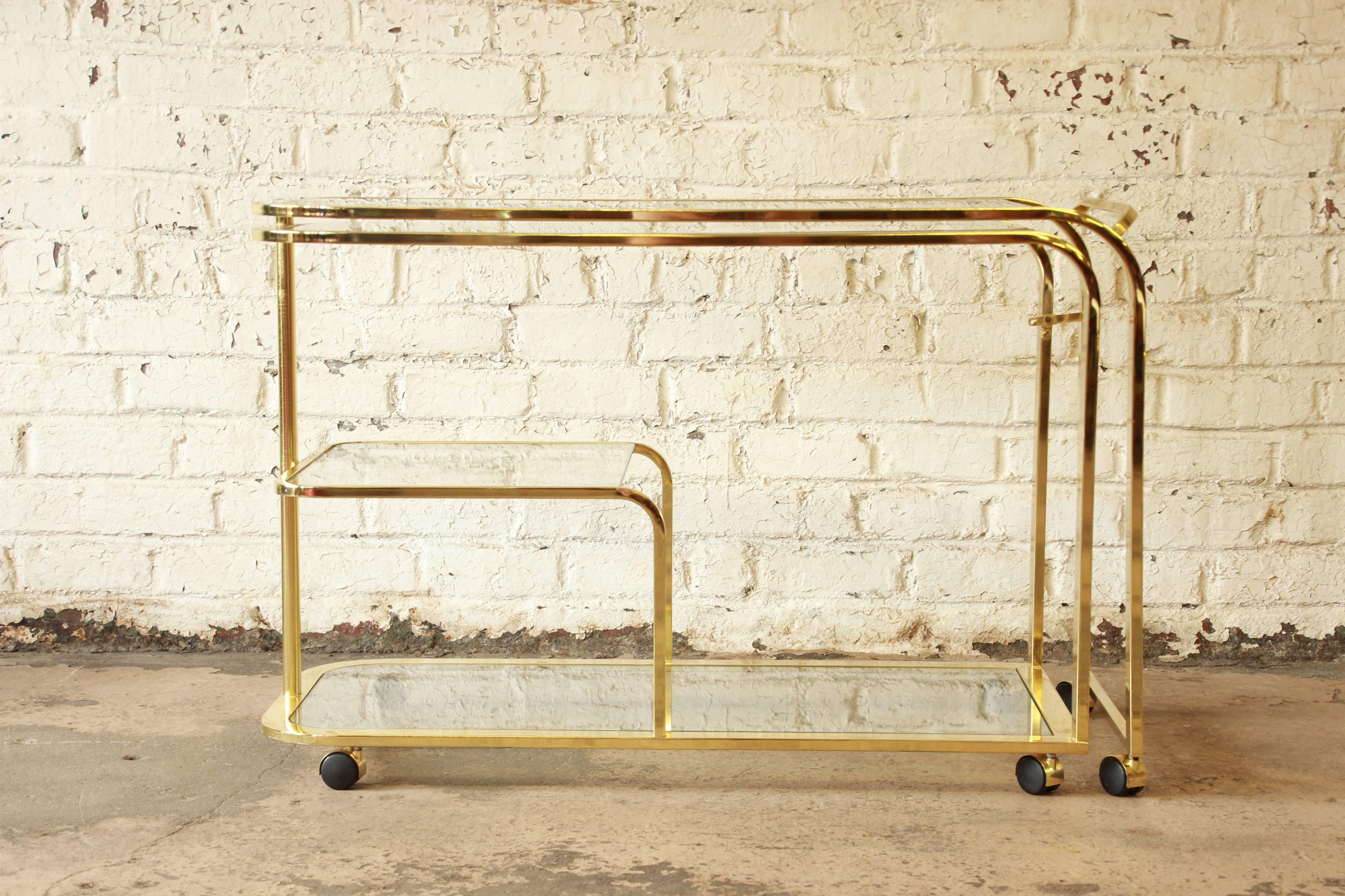 An exceptional 1970s Hollywood Regency brass and glass bar or tea cart by Design Institute of America. In the style of Milo Baughman. The three-tier cart uniquely expands into an L-shape or long bar and is 87
