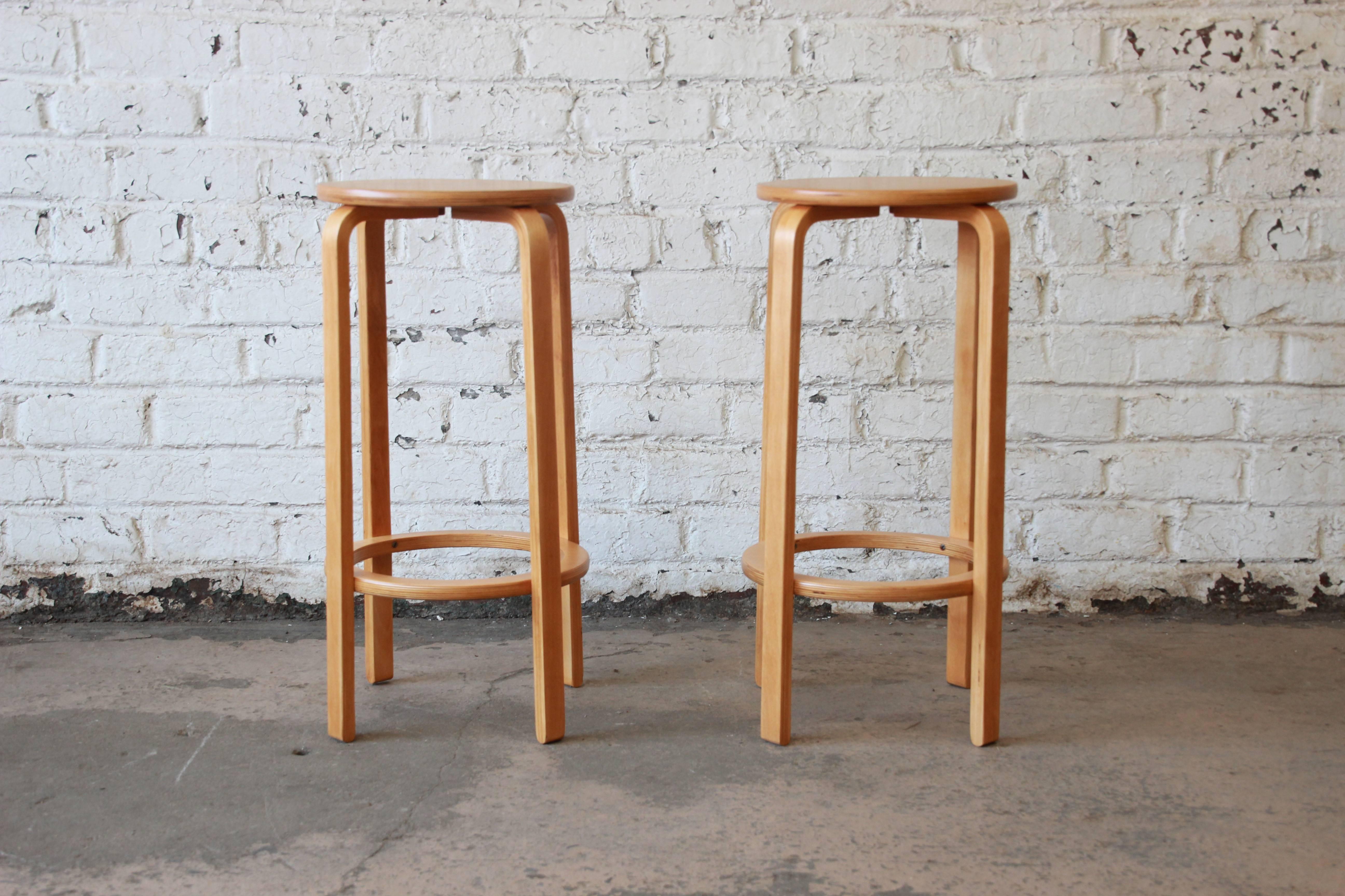 A gorgeous pair of model 64 bent birch wood bar stools designed in 1935 by iconic designer Alvar Aalto for Artek. The stools feature Aalto's signature bentwood design with sleek, Minimalist lines. They are sturdy and well-constructed. The stools