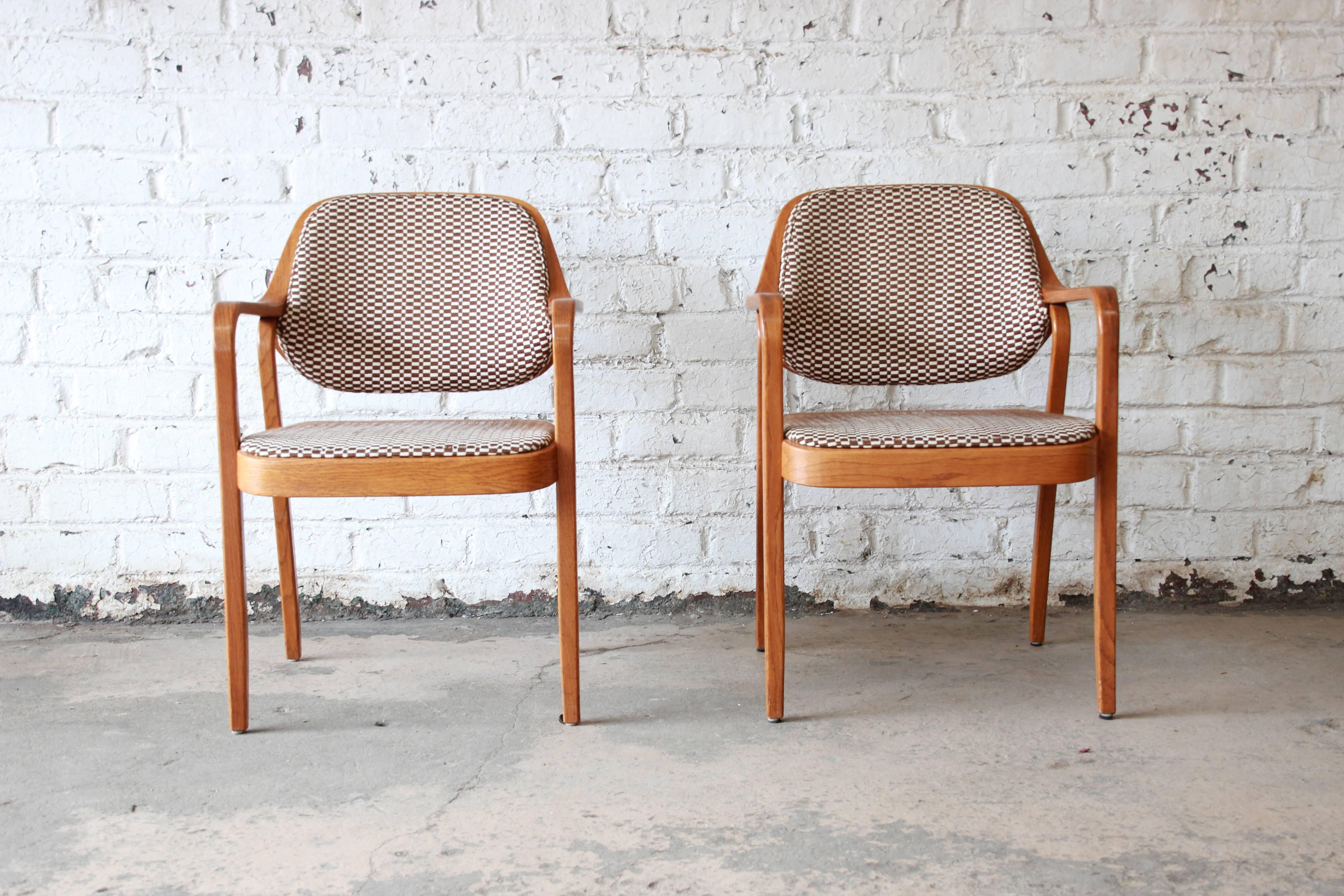 A sleek and stylish pair of Mid-Century Modern bentwood oak framed armchairs designed by Don Pettit for Knoll International. The chairs feature a solid oak frame with unique bentwood design and original brown and ivory checkered upholstery. The