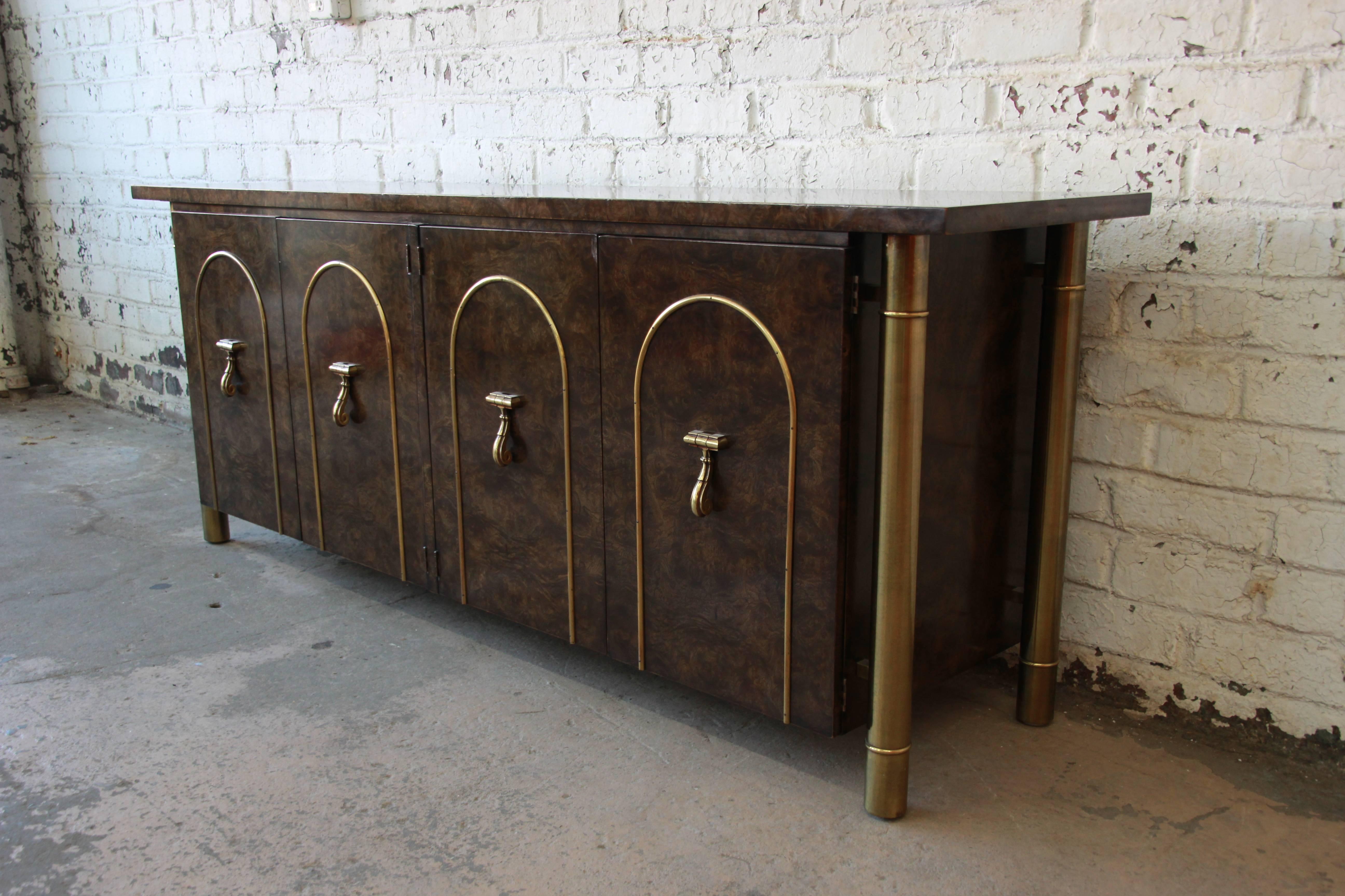 A stunning 1970s Mastercraft credenza or sideboard designed by William Doezema. The credenza features glossy dark burled Carpathian elmwood accented by brass arches and pulls on the four front doors and tall columned brass legs. Interior contains