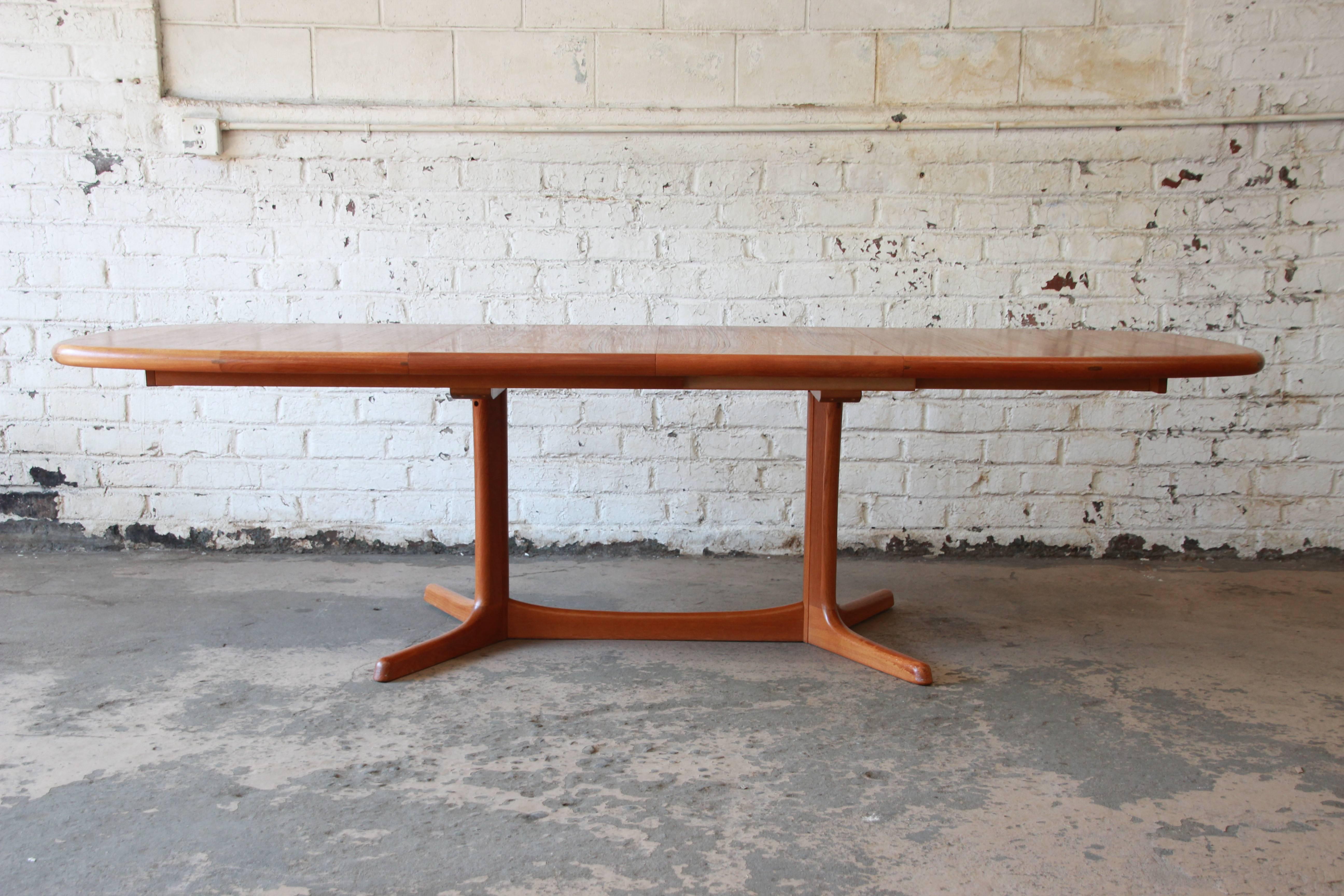A beautiful Danish Modern teak extension dining table by Dyrlund, circa 1970s. The table features gorgeous teak wood grain and a unique sculptural pedestal base. The table measures 64
