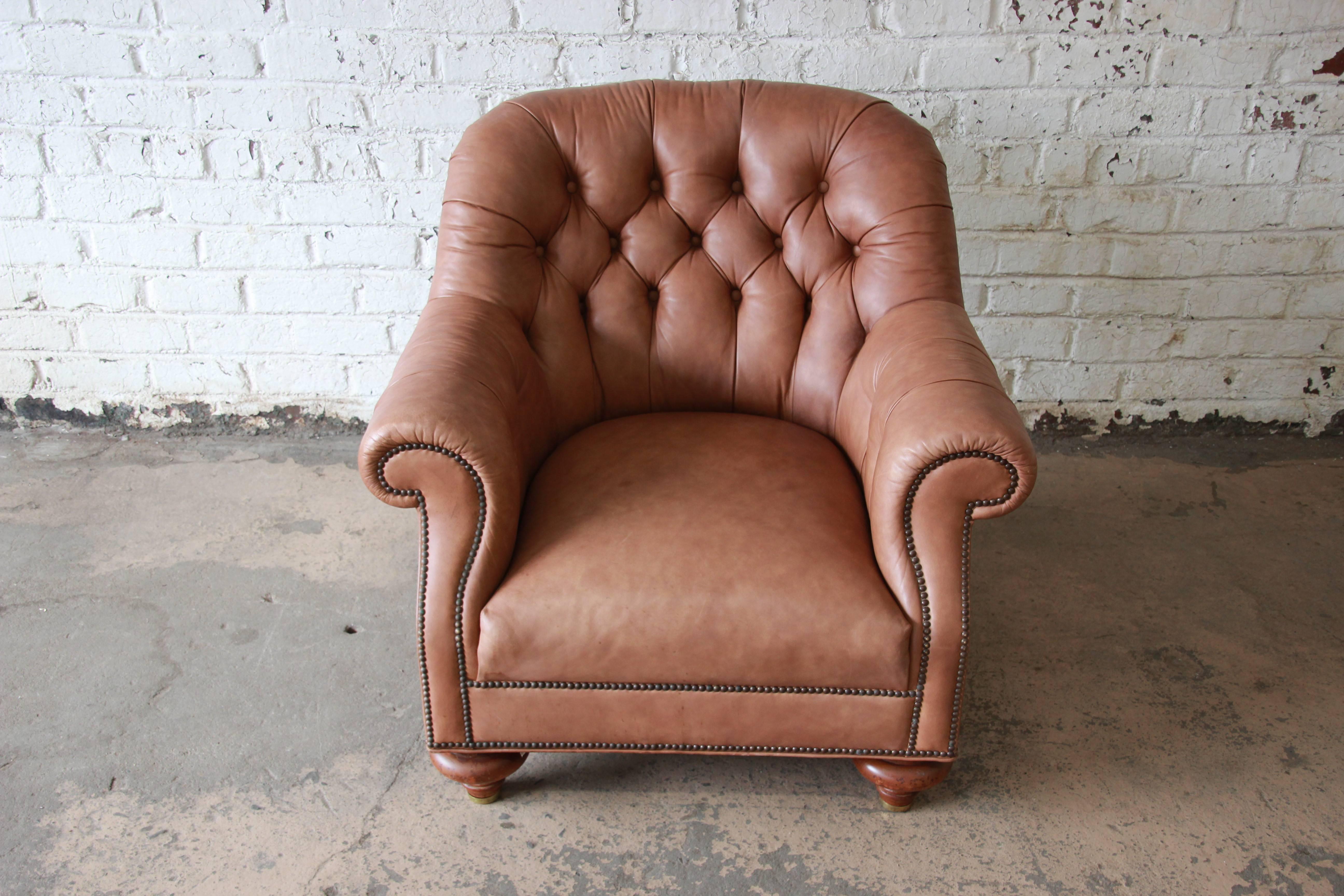 An outstanding leather Chesterfield style club or lounge chair by Baker Furniture. The chair features light brown tufted anilin leather upholstery, nailhead trim, and brass tipped solid maple wood bun feet. Very stylish, with a Classic English