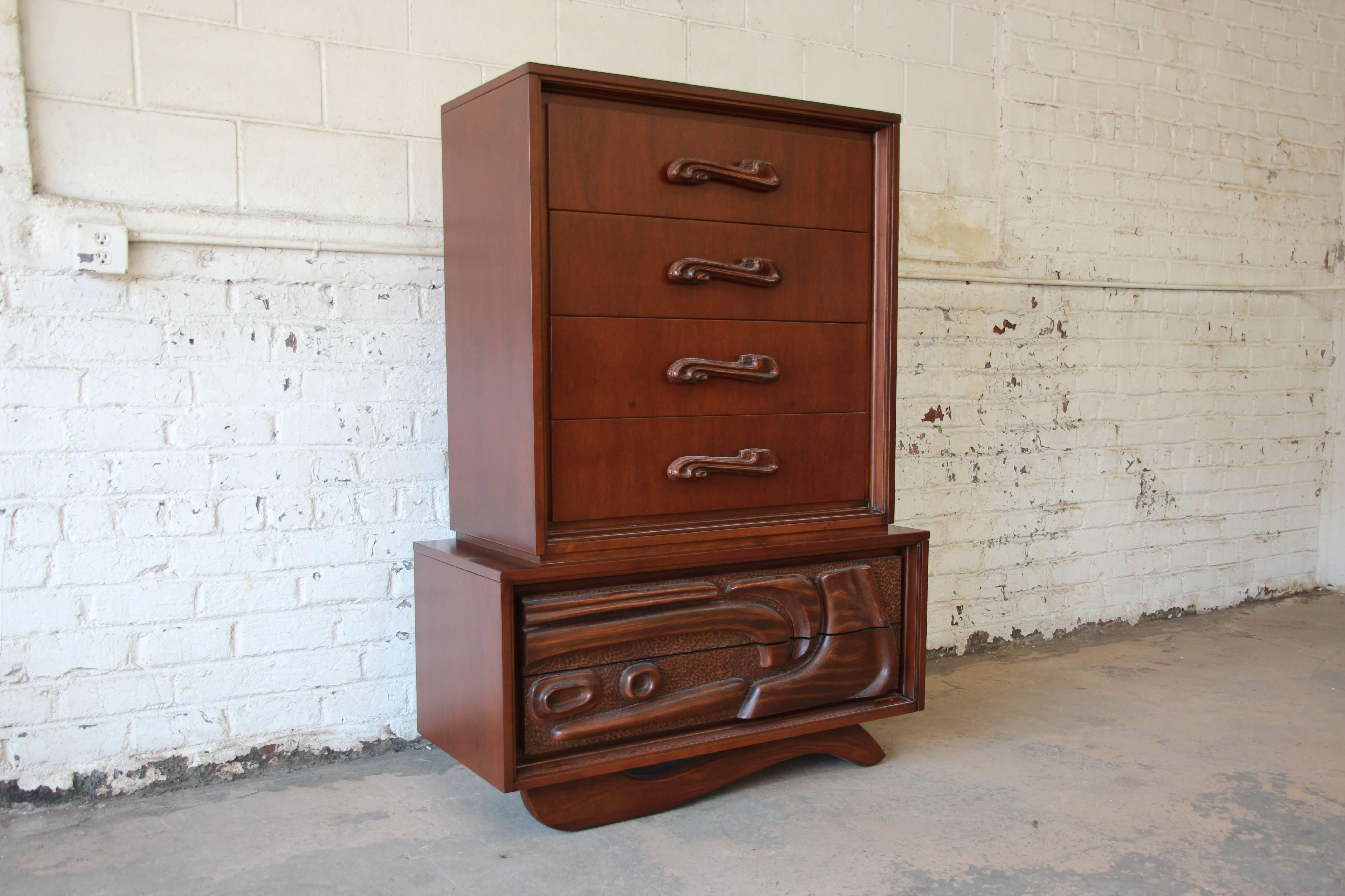 An outstanding Mid-Century Modern sculptural tiki highboy dresser by Pulaski. The highboy features stunning tropical mahogany wood grain and outstanding sculptural design, including the rare whale tail base. It has molded handles and panels that