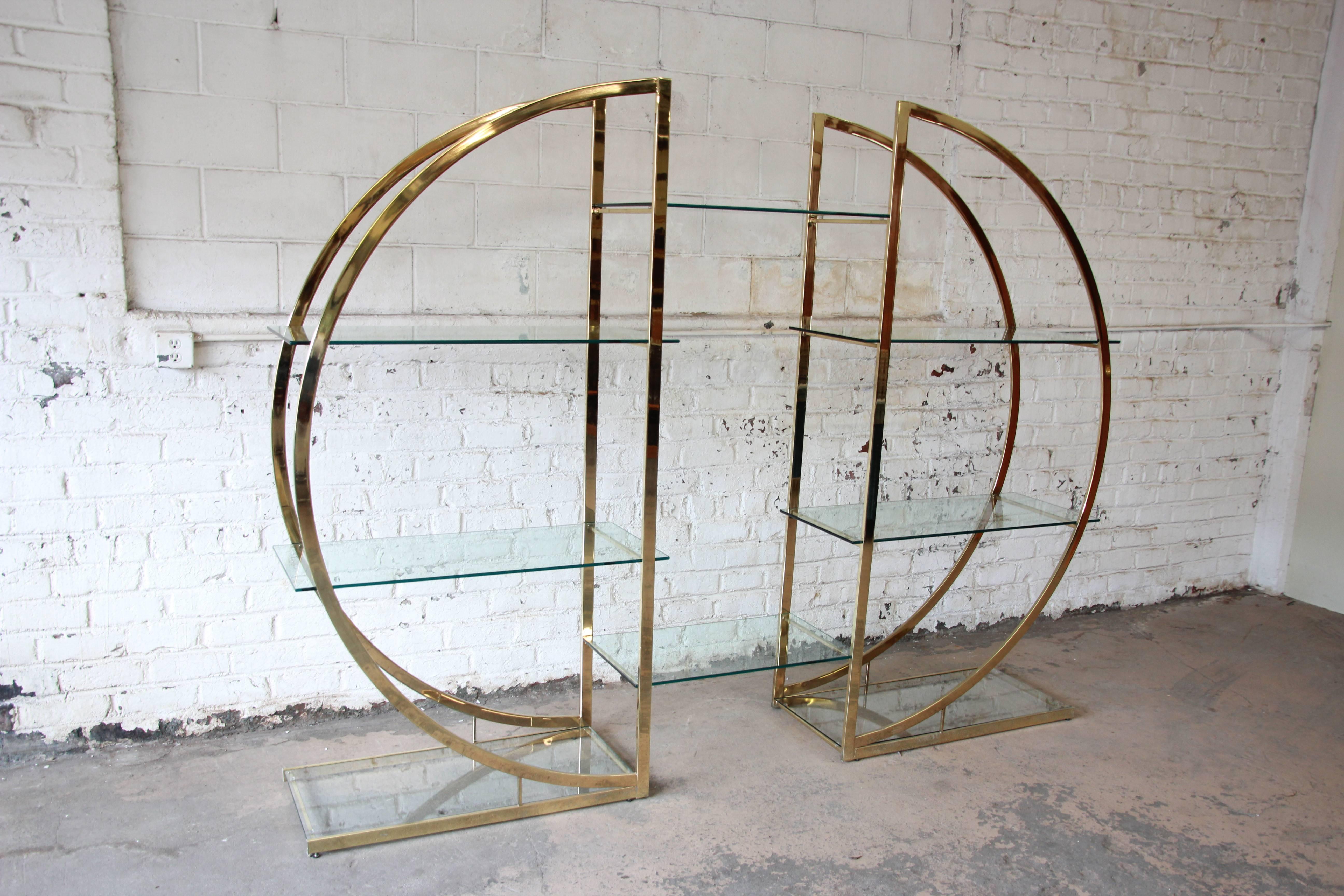 A stunning large modern circular brass plated étagère in the style of Milo Baughman. A pair of semicircle brass shelving units come together with eight glass shelves total. They can be used as two separate units by not using the center shelves or