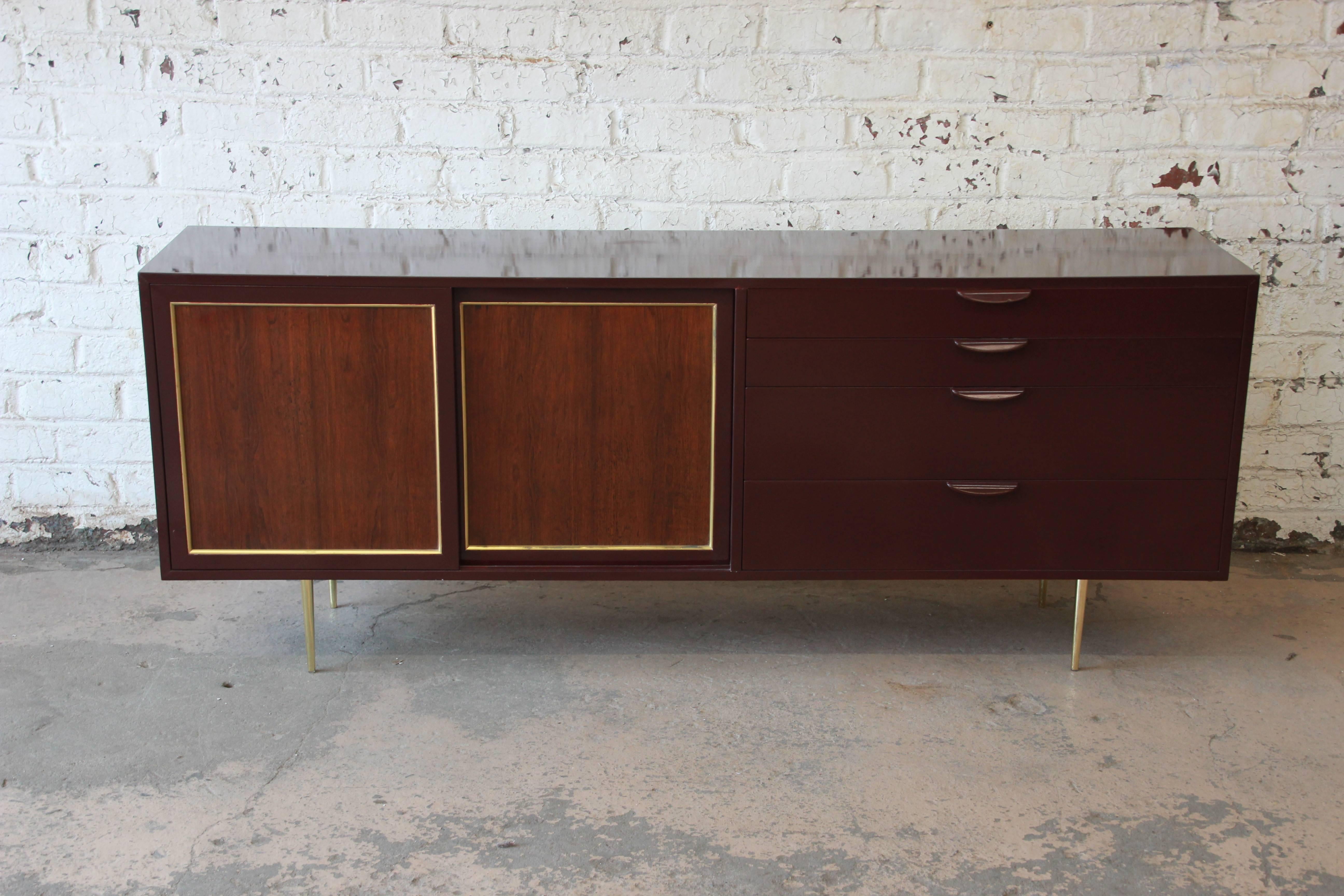 A sleek and stylish Mid-Century Modern credenza or dresser designed by Harvey Probber. The credenza features the original burgundy lacquered case, with sliding rosewood doors. The brass trim and slim brass feet give the credenza a sophisticated and