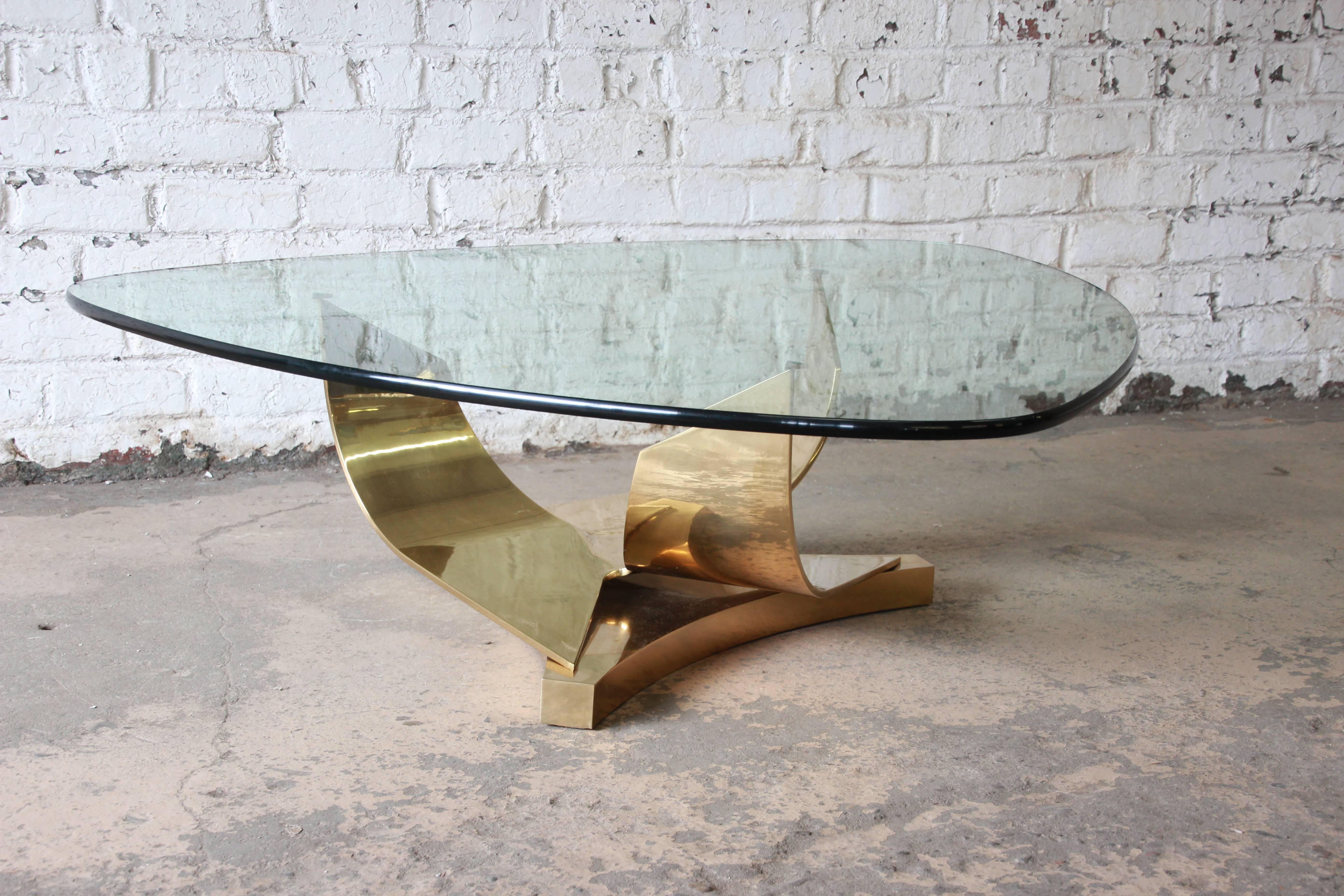 An outstanding sculptural brass and glass cocktail or coffee table designed by Ron Seff. The table features a stunning brass three-pronged base and a unique 3/4