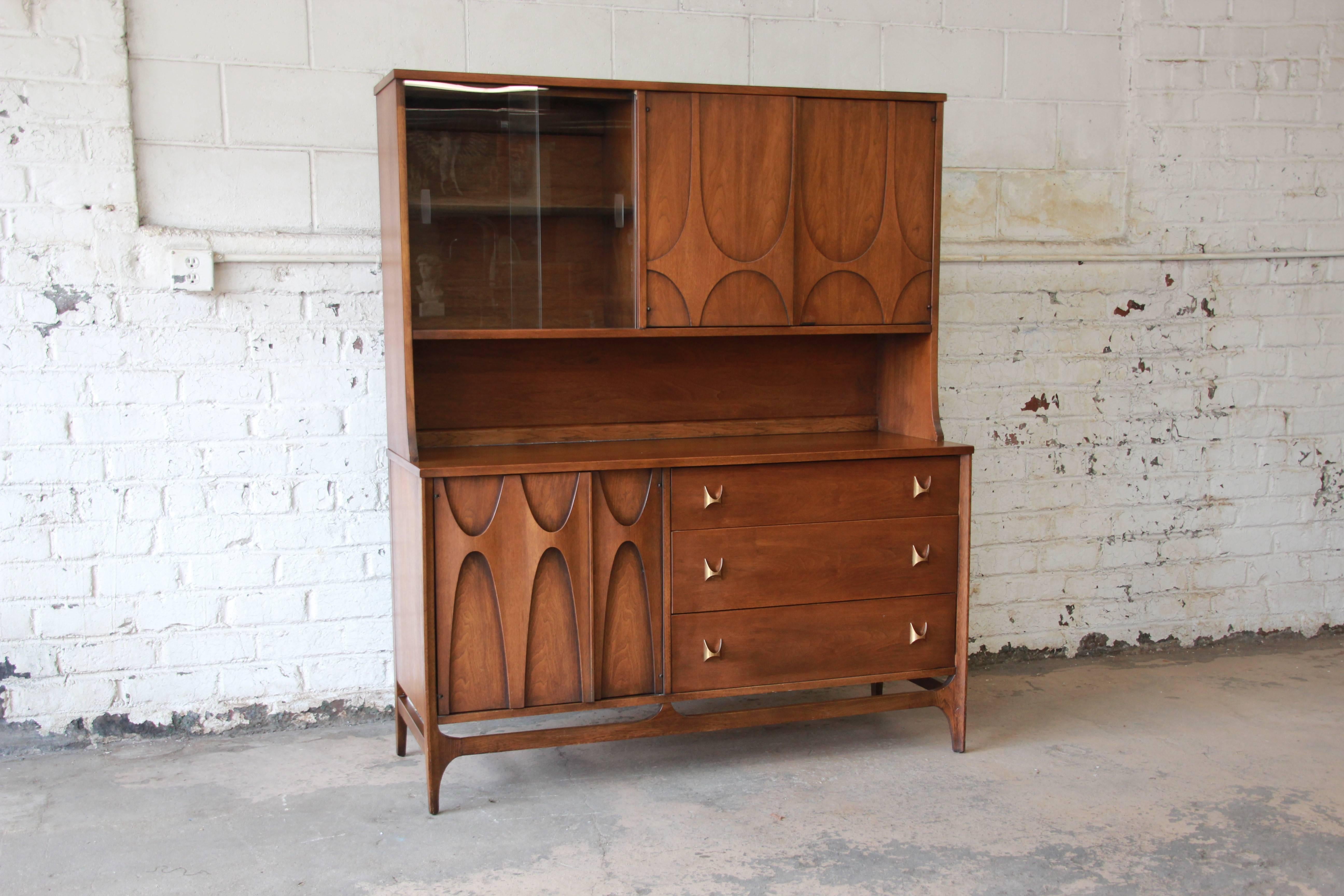 An exceptional Broyhill Brasilia Mid-Century Modern sculpted walnut sideboard with hutch. The sideboard features gorgeous walnut wood grain, with sculpted arches and original pulls. It offers ample room for storage with three deep dovetailed drawers