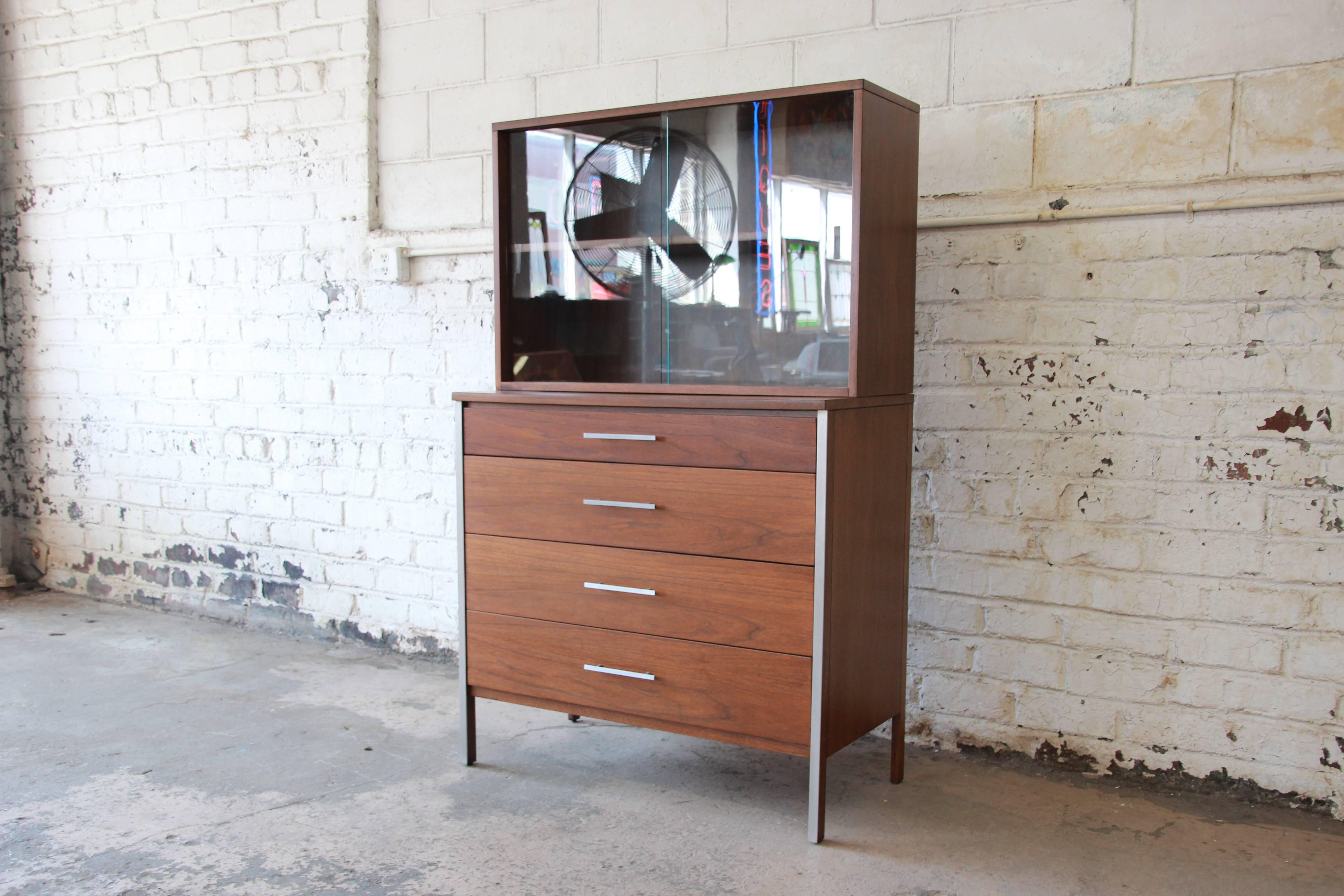 An exceptional Mid-Century Modern four-drawer walnut chest of drawers with glass front hutch top designed by Paul McCobb for Calvin Furniture. The chest features stunning walnut wood grain and sleek, Mid-Century design. The aluminum trim and drawer
