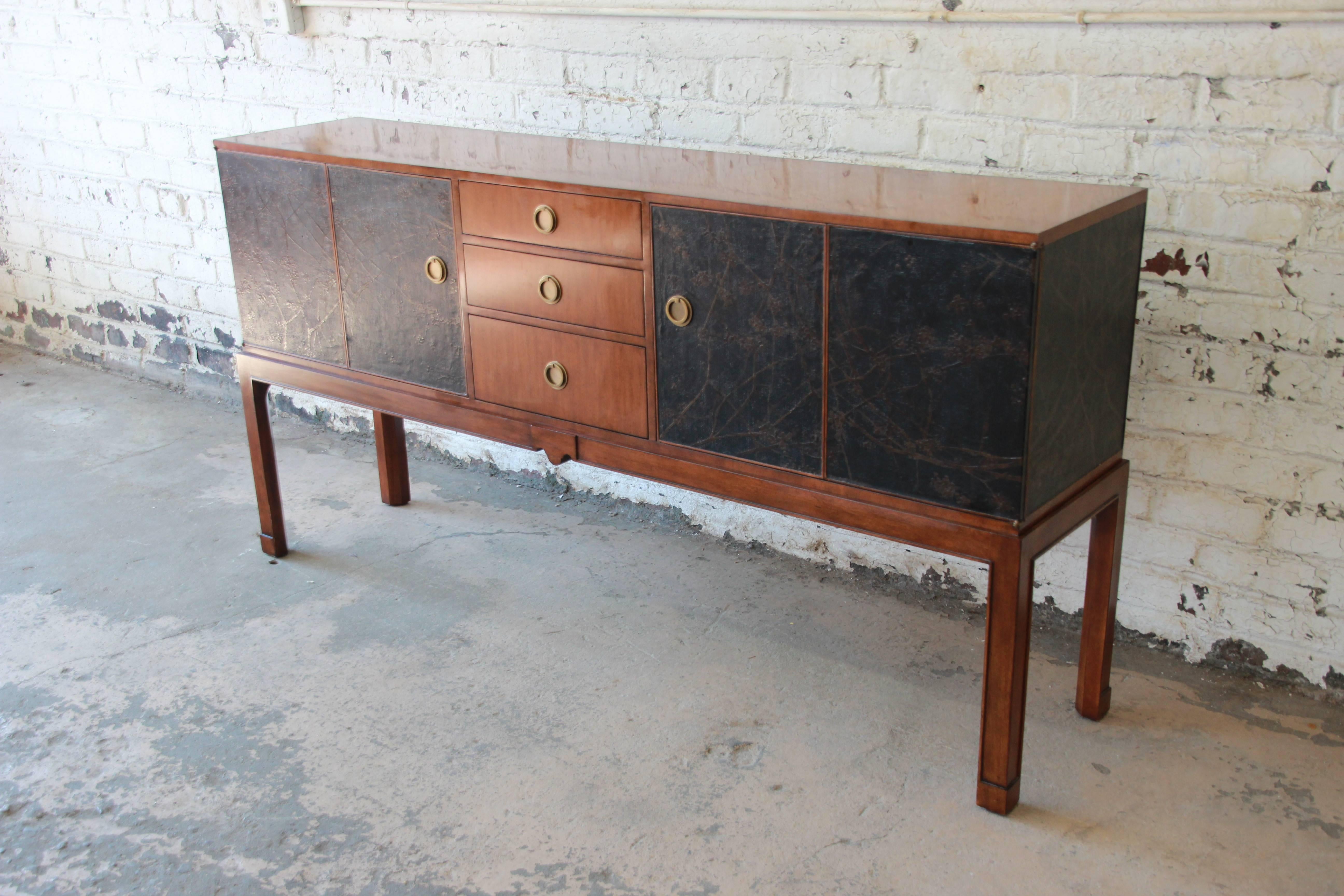A beautiful chinoiserie sideboard in walnut by Theodore Alexander. The rectangular top above a central bank of three graduated drawers, flanked two each side by a chinoiserie painted and black canvas wrapped double hinged door, each enclosing an