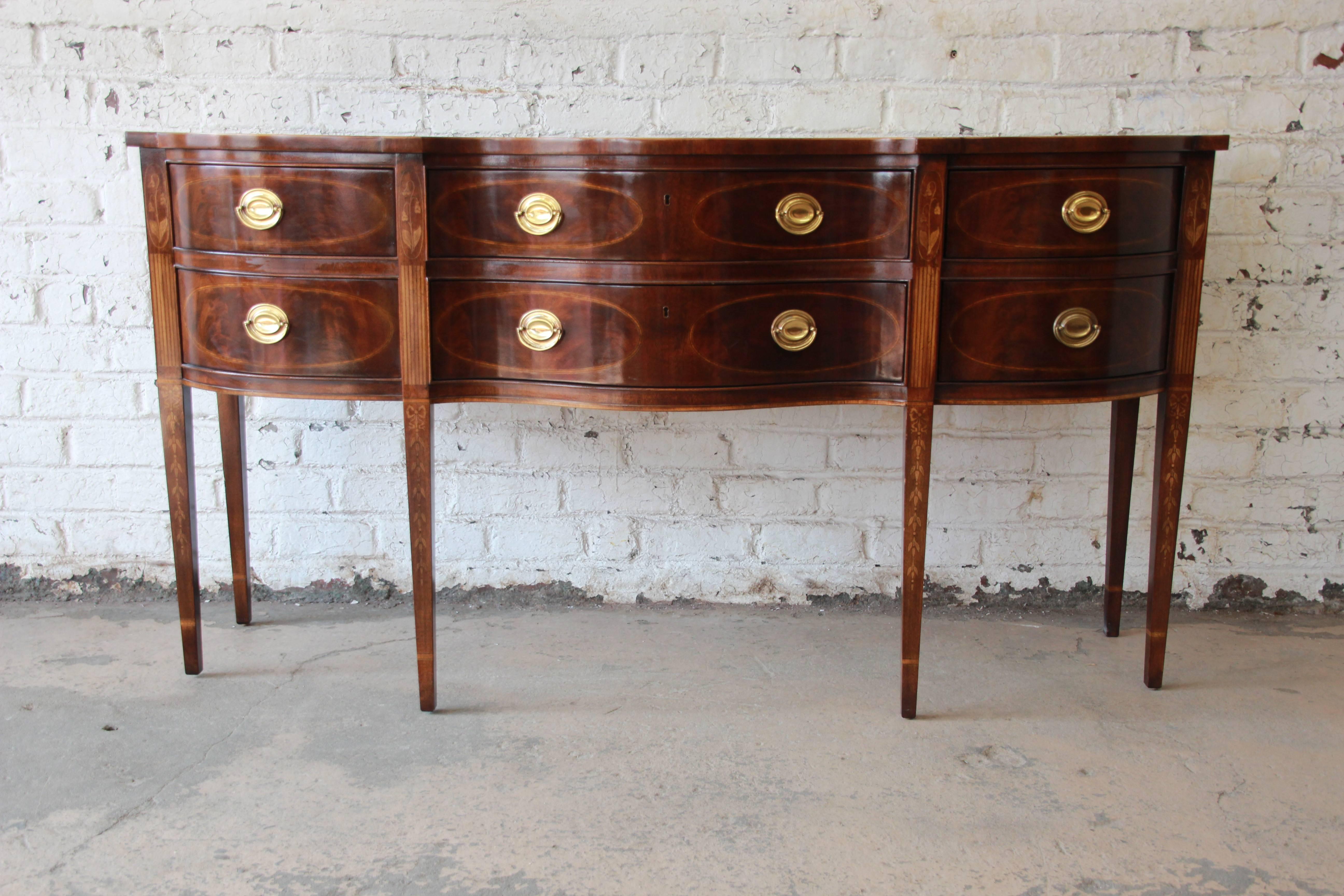 An exceptional inlaid mahogany Hepplewhite style sideboard from the Heirlooms collection by Drexel Heritage. The sideboard features beautiful flame mahogany wood grain and fine inlaid details. It offers ample room for storage with six deep