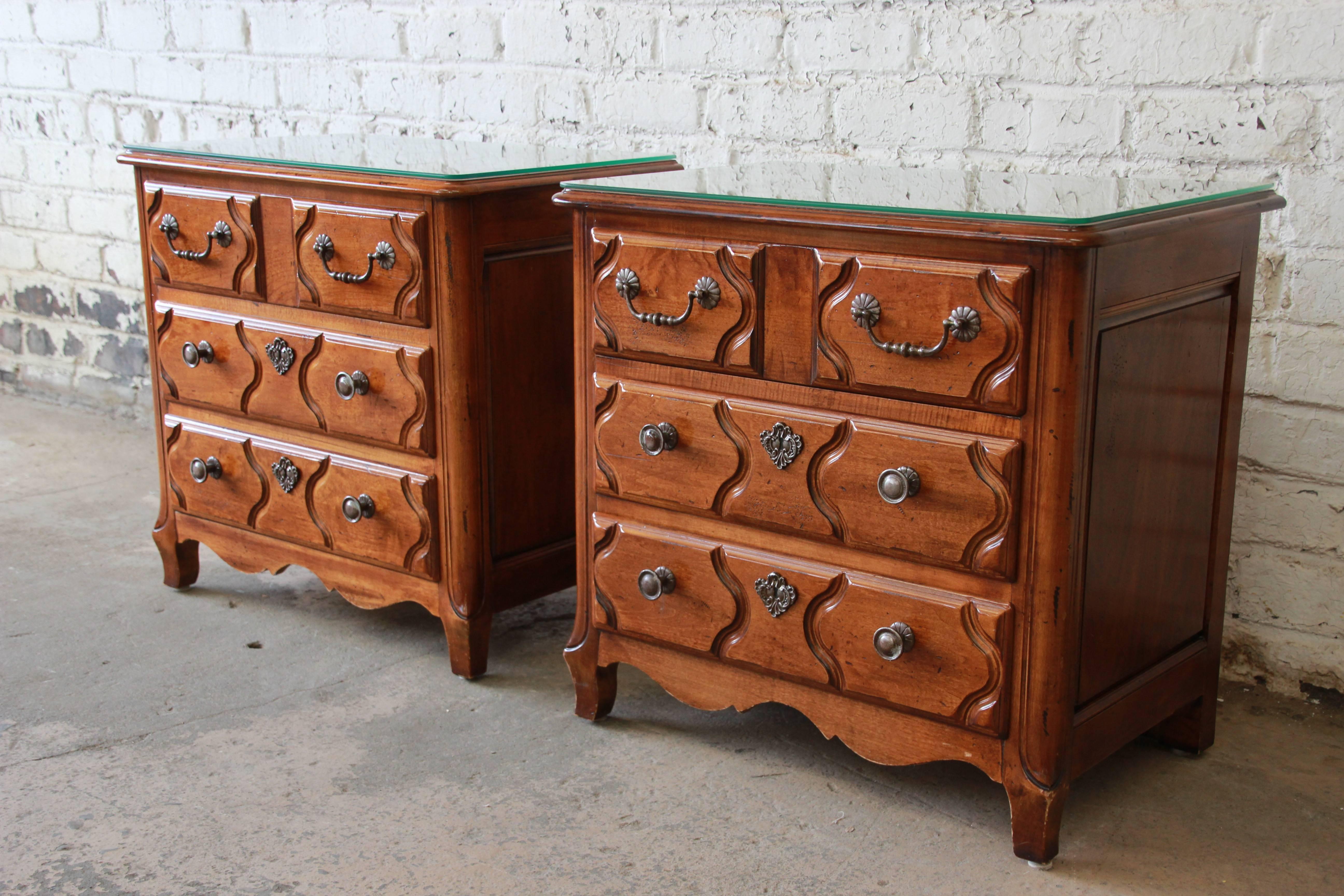 A gorgeous pair of solid cheerywood three-drawer chests or nightstands from the Pierre Deux French Country collection by Henredon. The chests feature stunning carved wood details and original hardware. They offer ample room for storage, each with