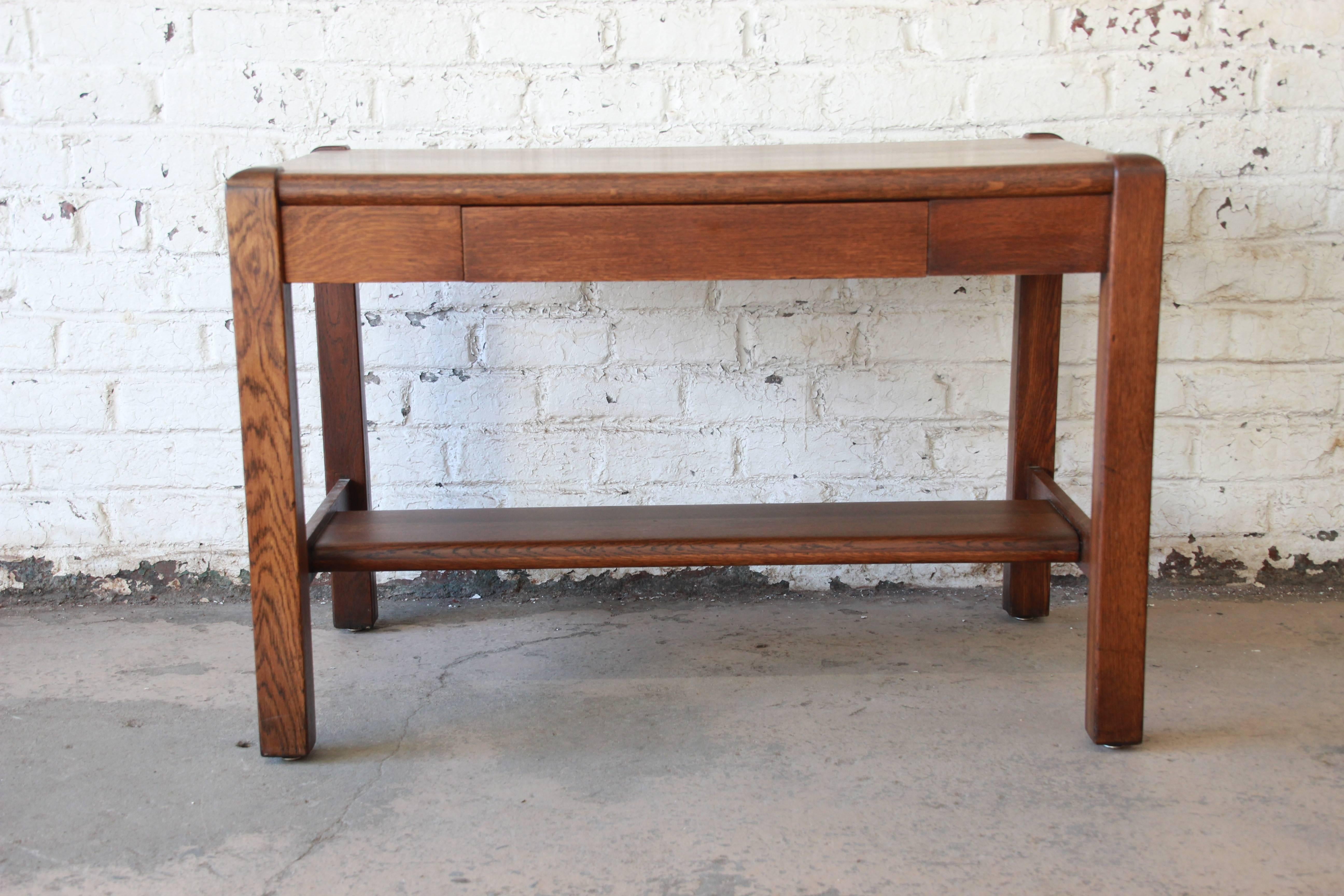 A beautiful antique American Arts & Crafts period Mission oak writing desk. The desk features solid wood construction, with gorgeous quarter sawn oak wood grain. It has a single dovetailed drawer and a stretcher between the legs. It is finished on