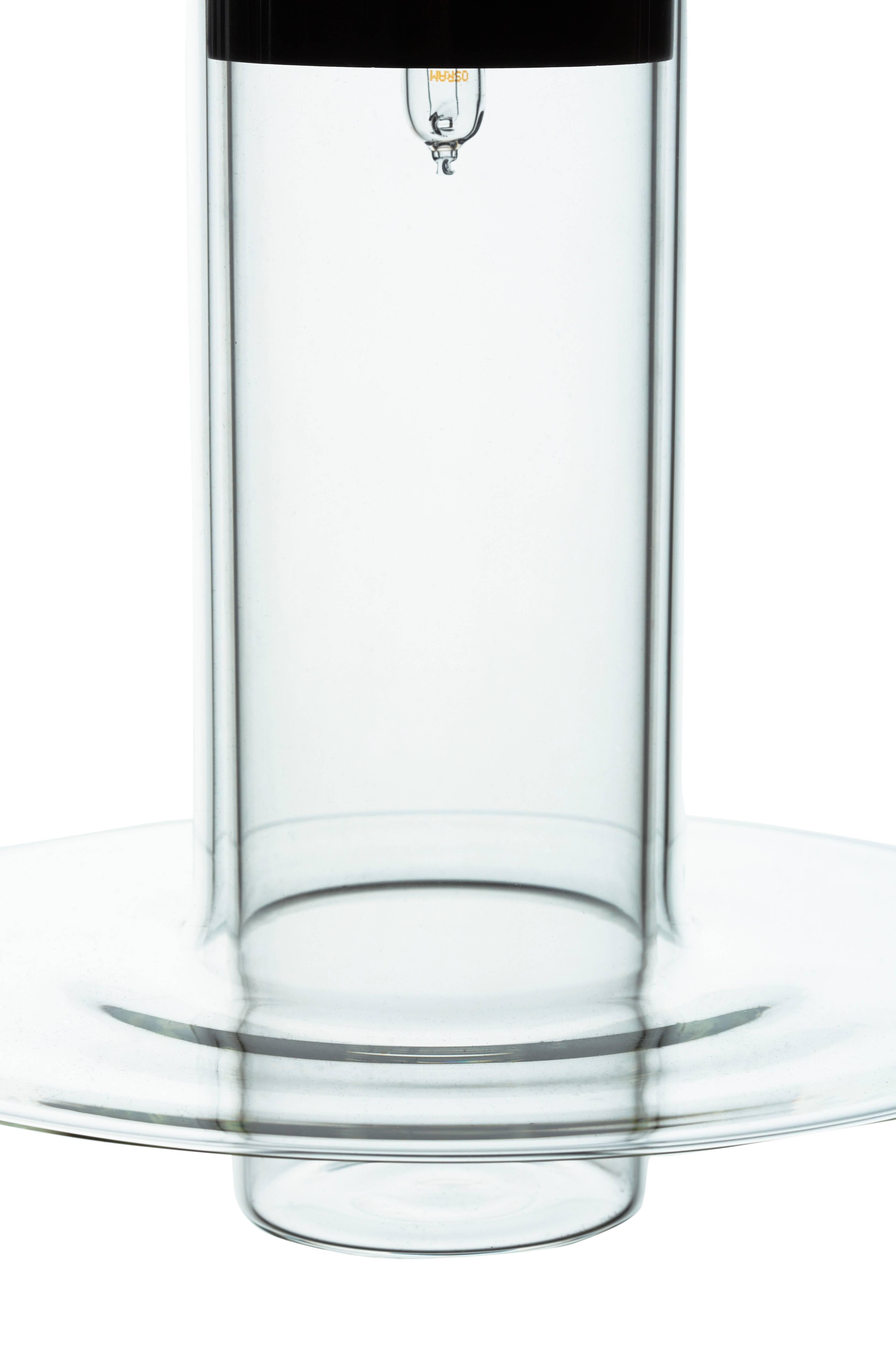 Le design de Pawson place un cylindre de verre fabriqué à la main à l'intérieur d'un autre, le cylindre extérieur s'évasant en une lèvre discale raffinée sur son bord inférieur. La lampe projette la lumière vers le bas, mais son corps transparent