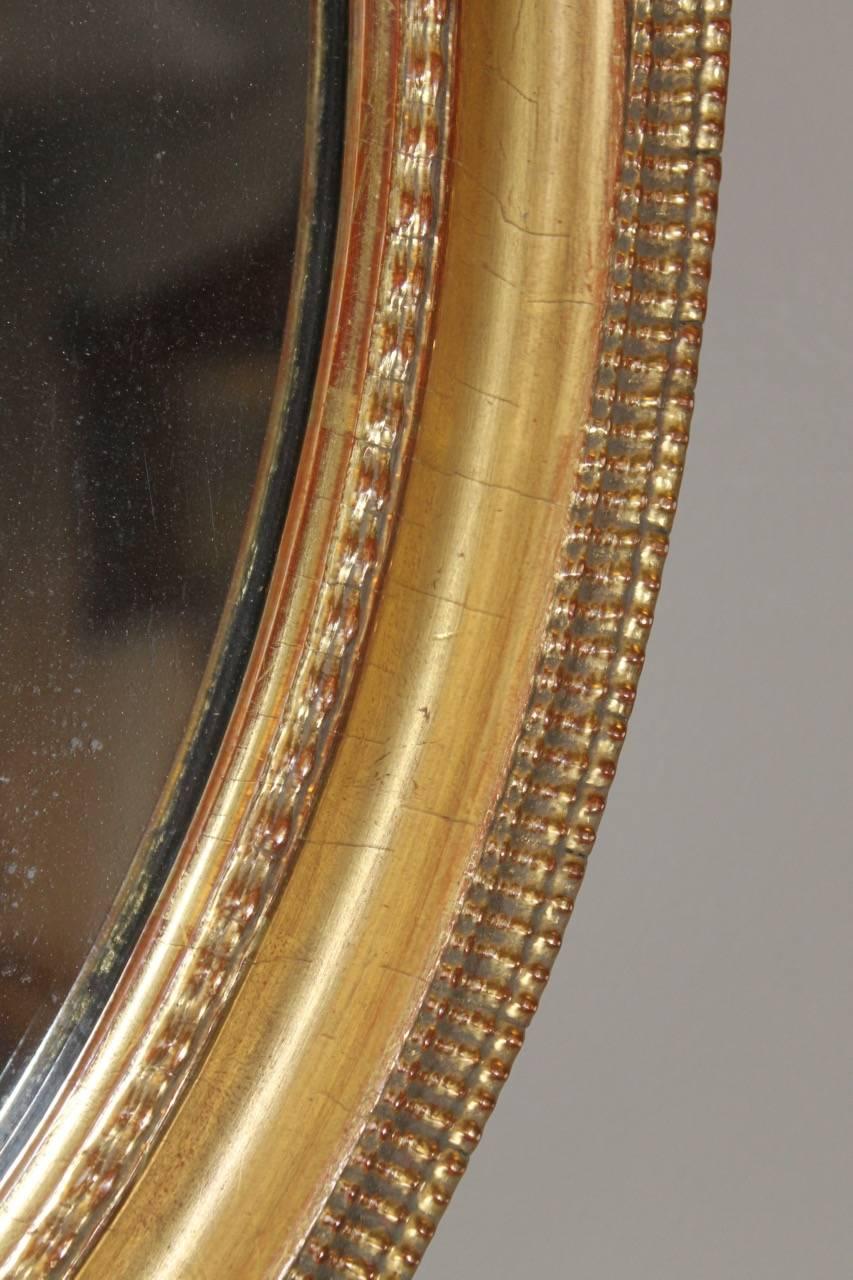 A very attractive oval mirror of pleasing color and design, retaining its original mercury mirror plate. The top edge consists of an applied composition ripple design of good crisp quality. The water gilded finish has worn through evenly to show a