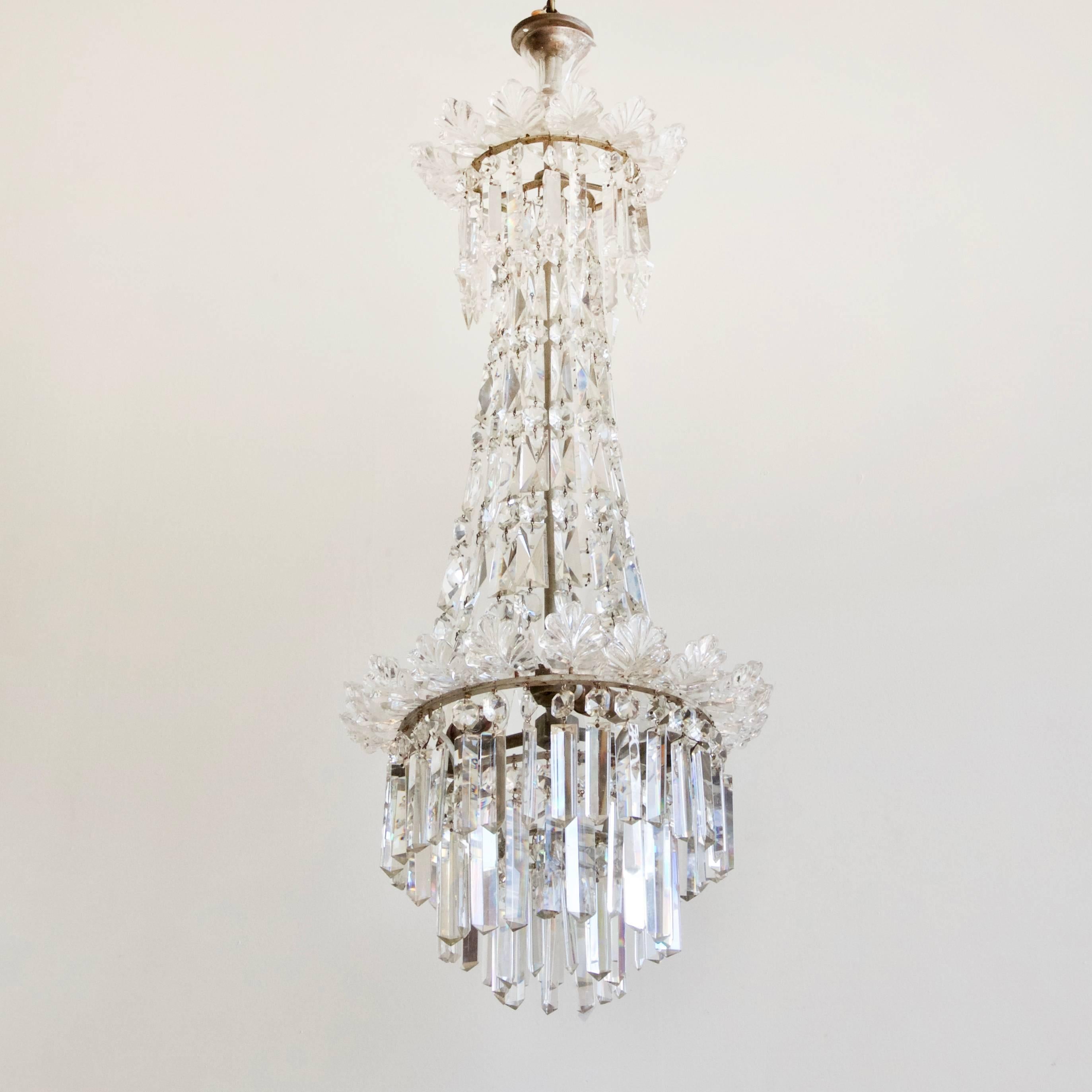 A tall elegant English chandelier dressed in hand-cut crystal. A ring of Prince Albert cut crystal are hung from an upper tier of crystal leaf pieces. Swags of coffin lid and buttons form the central body leading to a waterfall of crystal prism