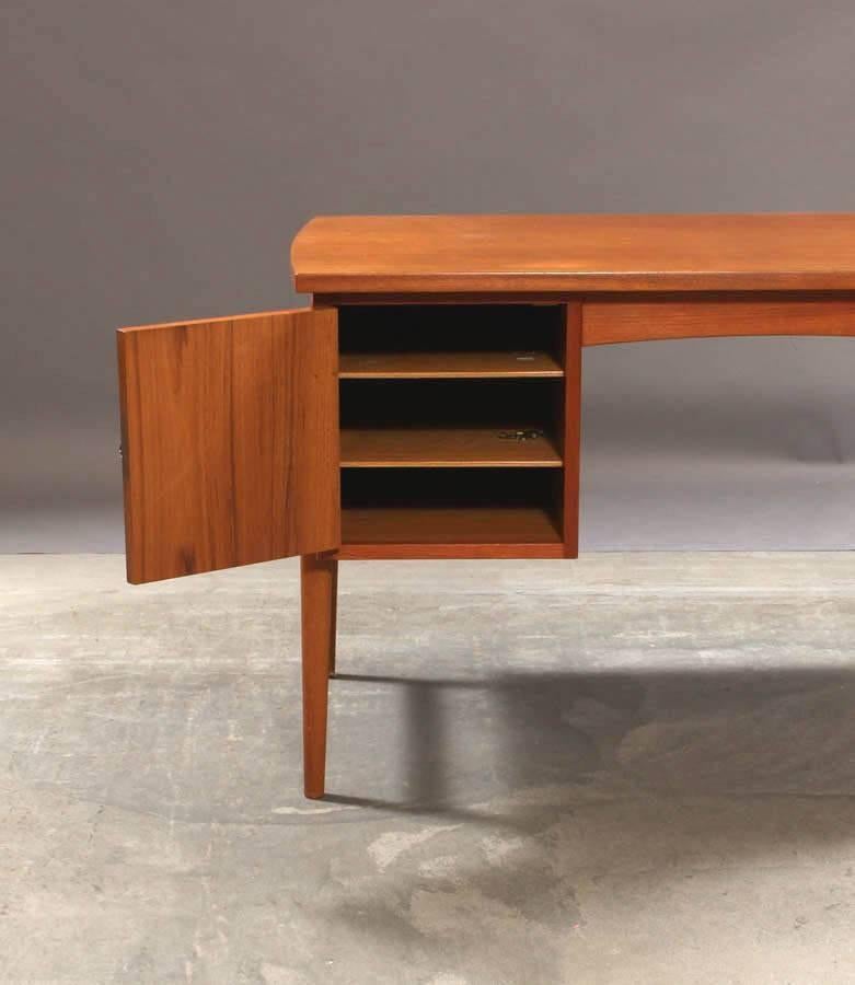 Danish furniture manufacturer. Freestanding desk in veneered teak wood and solid legs and handles. Front with three drawers and one door with key. 

 