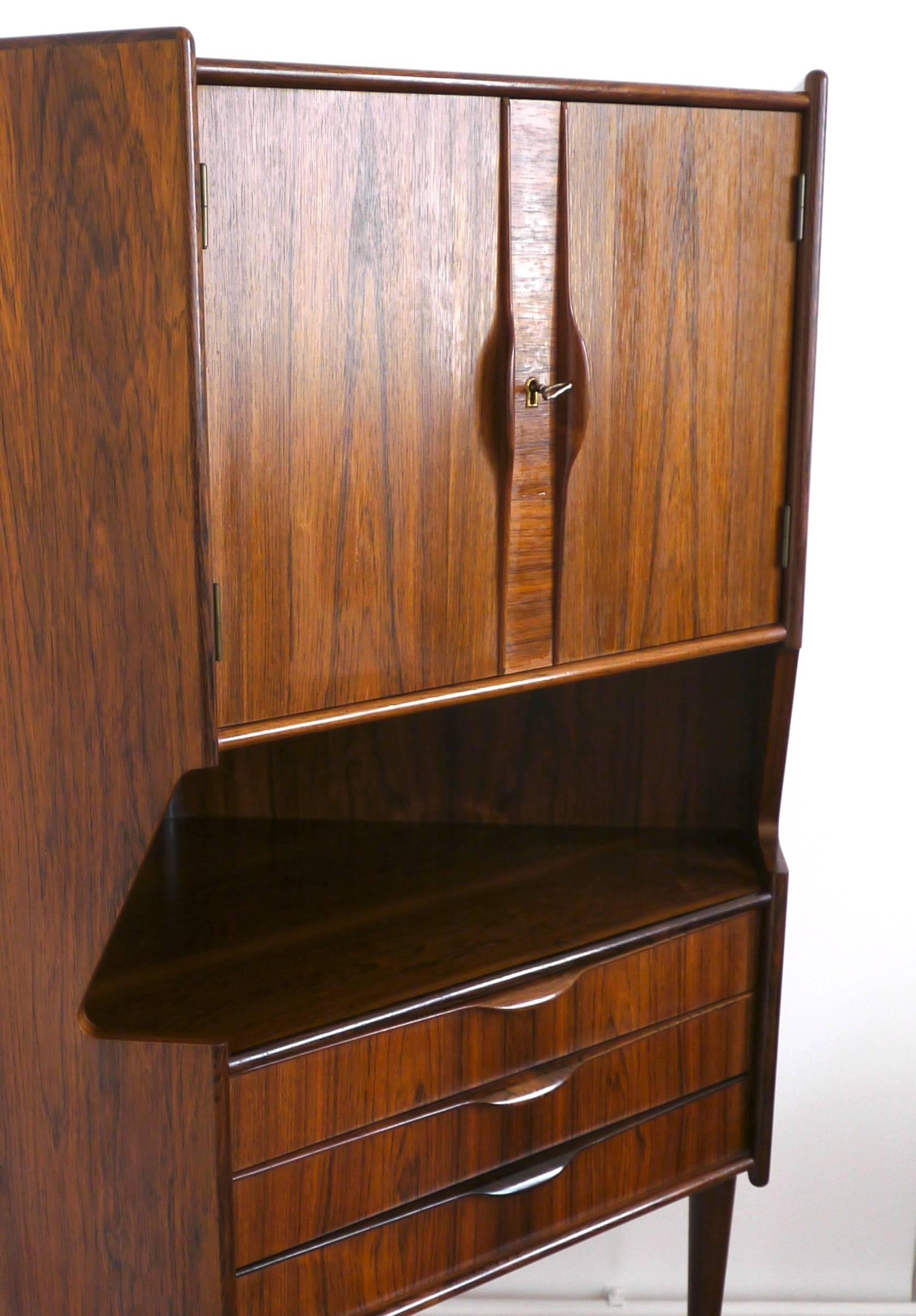 This corner highboard features a cocktail bar, two doors and three drawers. It is made of veneered Rio Palisander and shows a shiny lacquered finish with an amazing wood grain. A very stylish and elegant look! The legs and handles are solid wood.