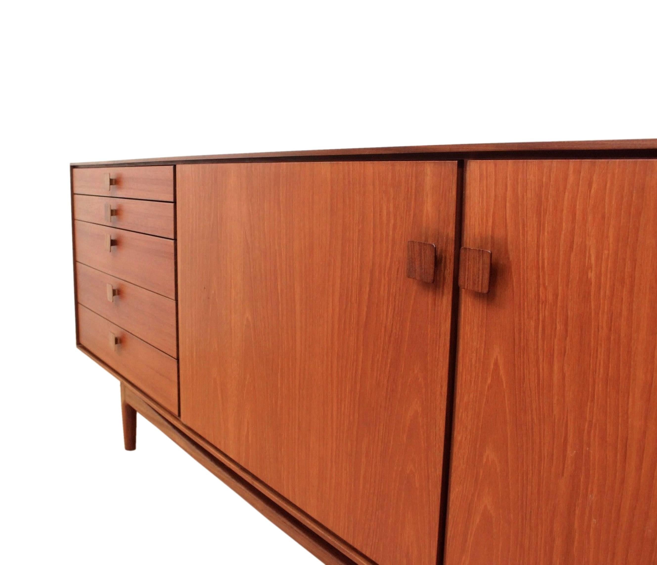 A very Classic Mid-Century piece: This long sideboard offers plenty of storage in the interior cavities with two cupboards each have one adjustable shelf. It is made of teak wood and afromosia handles. Ib Kofod-Larsen has designed it in the 1960s