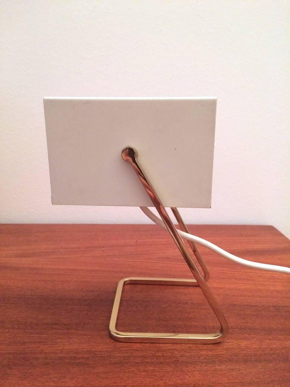 This cube desk lamp, model 45097 / 012, was made by Kaiser Leuchten in the 1960s. It features a white metal shade set on a brass frame. It is fully functioning and takes one 25W E14 bulb.