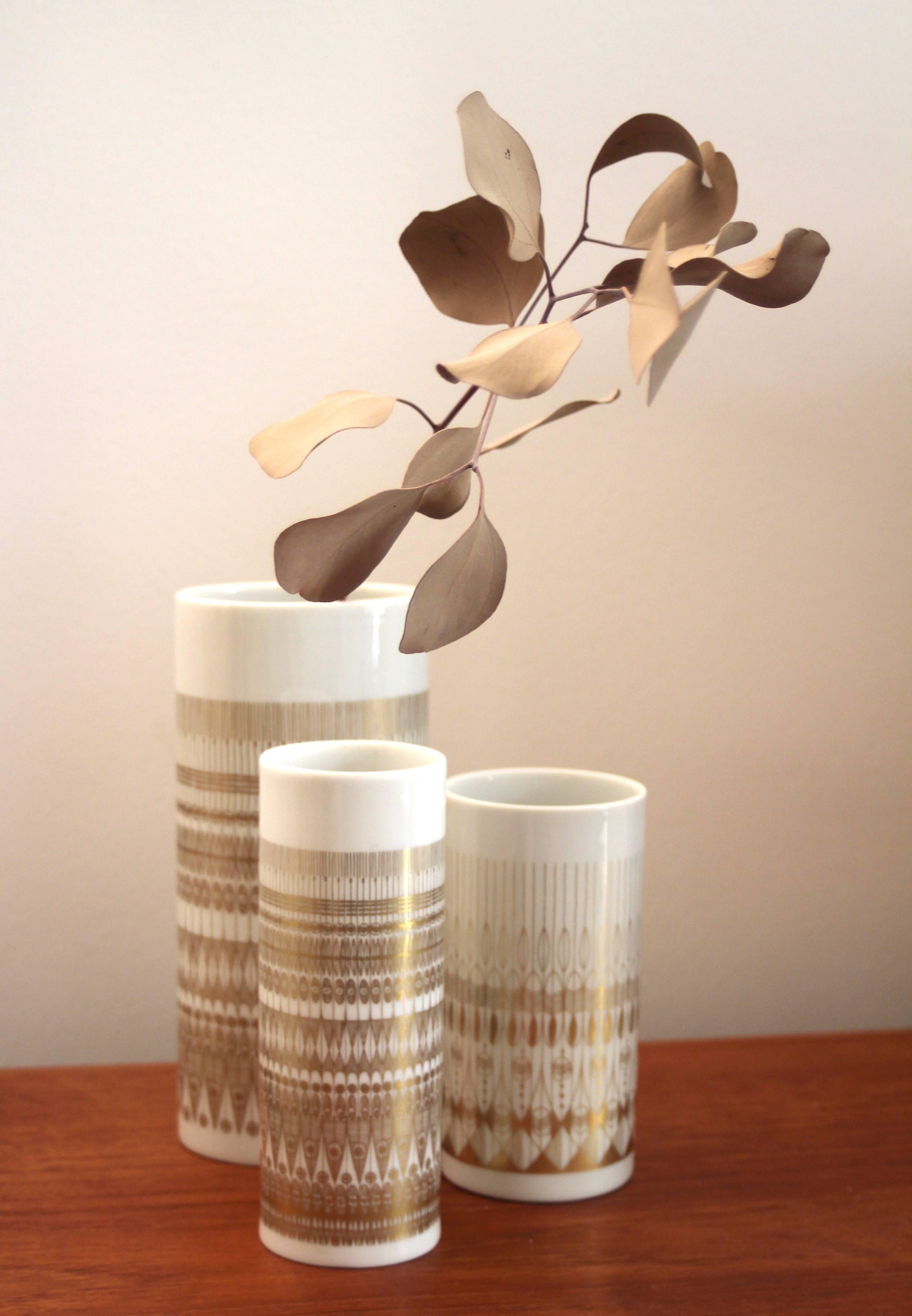 A stunning set of midcentury vases, designed by Hans Theo Baumann for the German porcelain manufacturer Rosenthal, produced around the 1960s-1970s in Germany. It features graphic op-type color print in gold on white lacquered porcelain.
