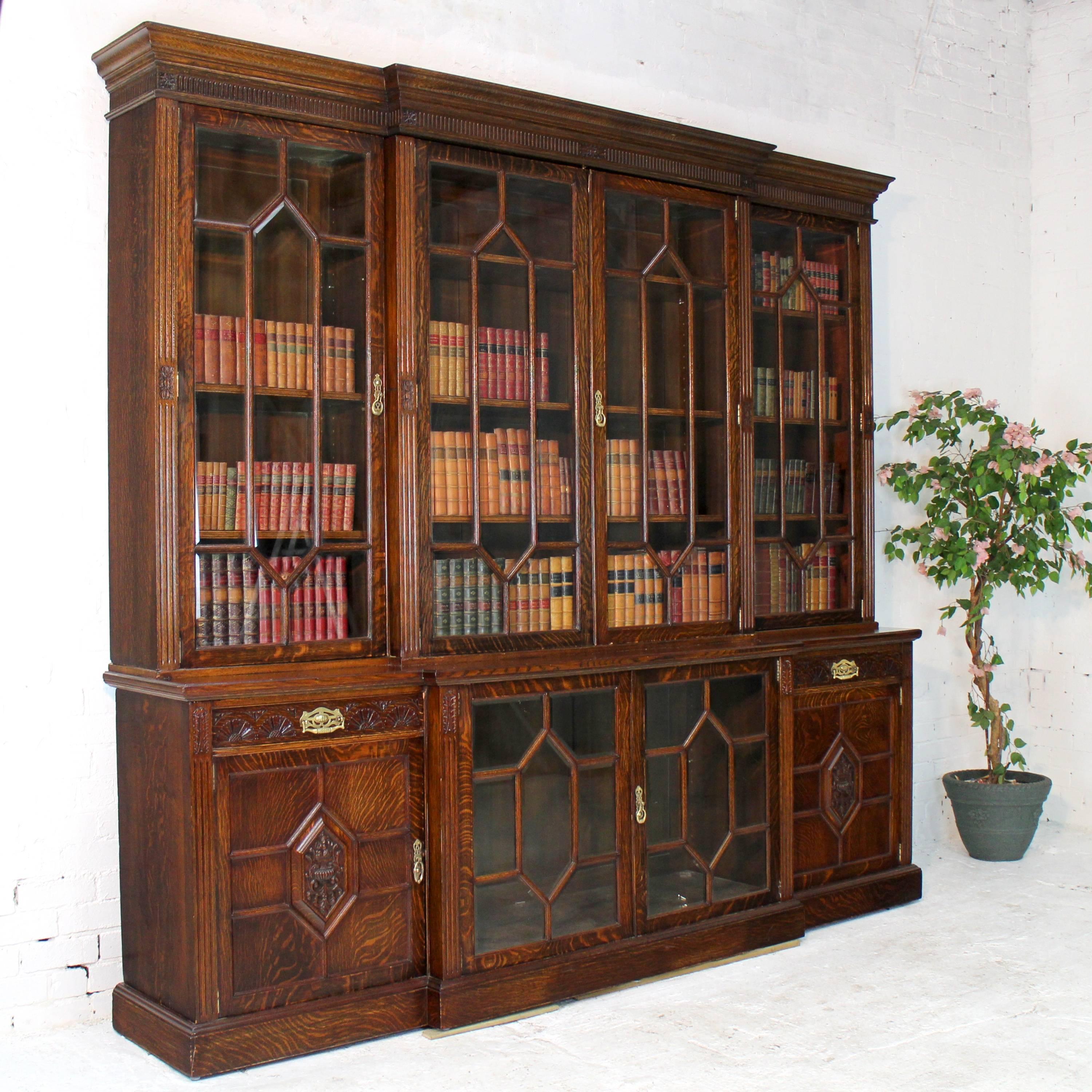 A stunning Victorian four-door breakfront bookcase by Maple & Co in the Aesthetic/Arts & Crafts style and dating to circa 1889. In quarter sawn oak with bevelled glass panes to the astragal glazed doors it features foliate carved emblems and fluting