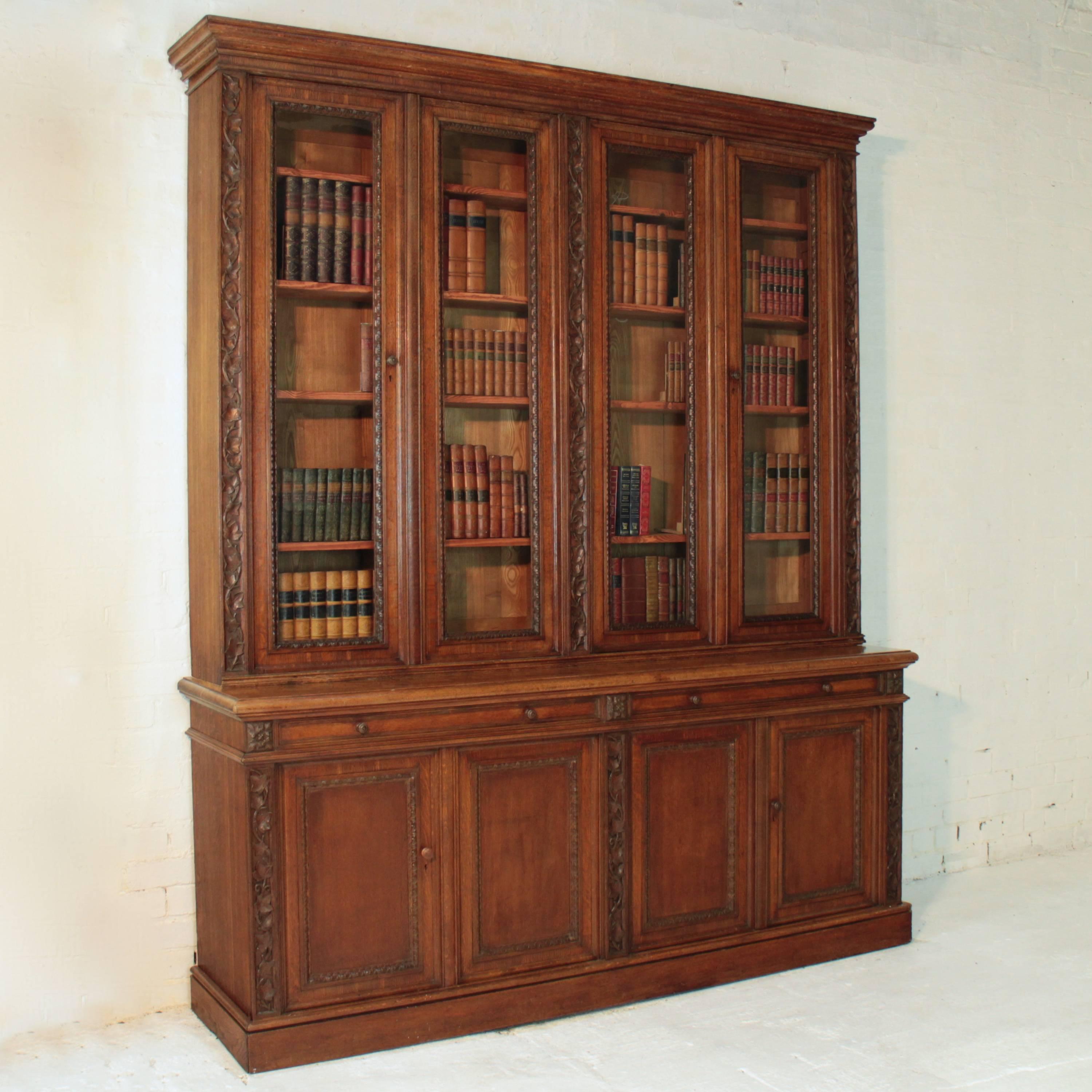 A beautiful Victorian four-door library bookcase with carved panels of climbing ivy and a parquetry veneered top. It has carved mouldings to the four glazed doors, two imitation drawers and four fielded panel doors below. Fitted with wooden knob