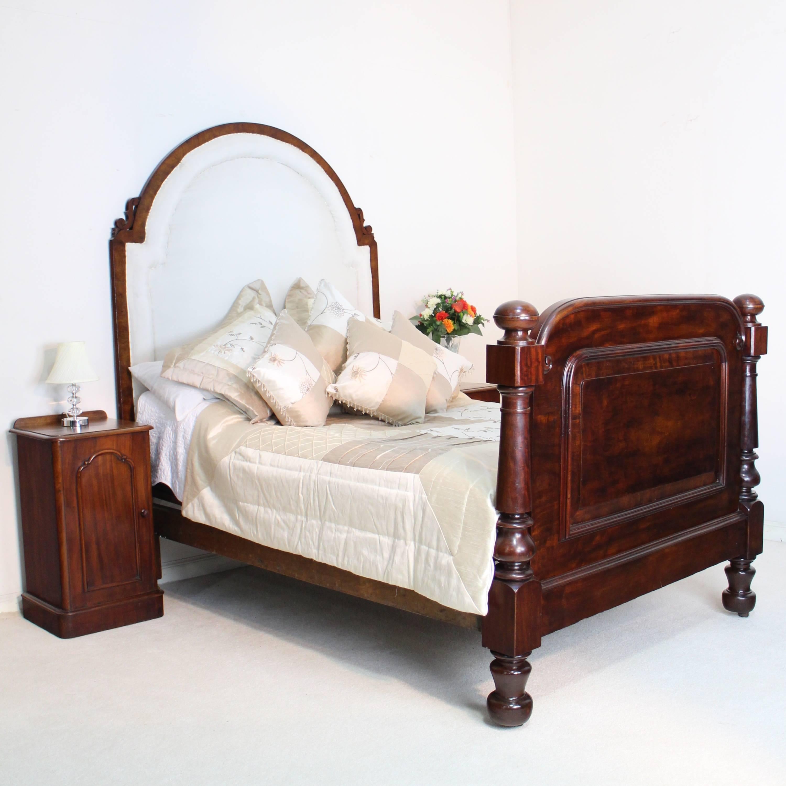 A handsome Scottish Victorian mahogany and upholstered double bed frame with a tall arched and padded headboard with carved s-scrolls. The footboard features large block and turned columns on bulbous feet with hidden castors and a beautifully