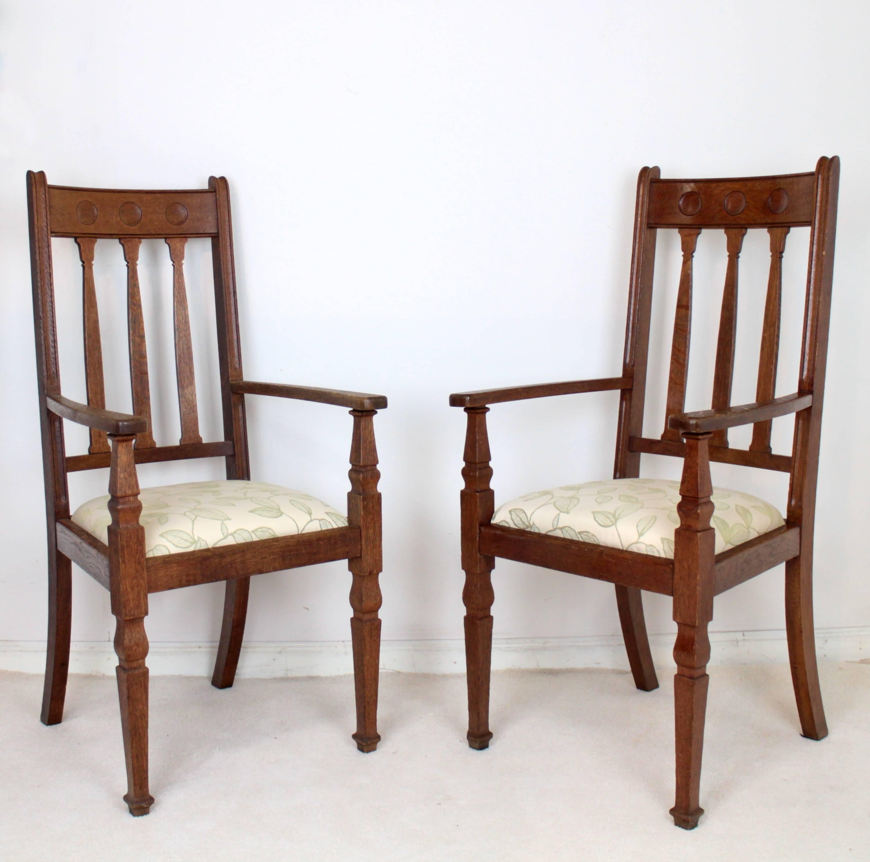 A super pair of Arts & Crafts oak open armchairs by Shapland & Petter of Barnstaple and dating to circa 1910. With three roundels to the toprail and tulip shaped splats beneath, they have wide out-curved armrests and square vase shaped tapering
