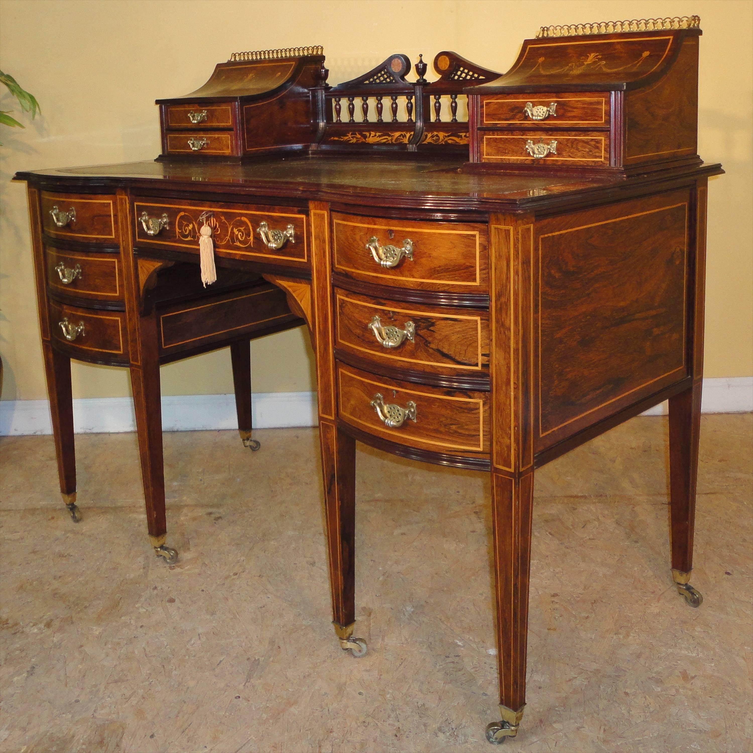 A superb quality late Victorian Sheraton style rosewood and marquetry desk in the manner of Edwards & Roberts. With a Carlton House influenced top featuring elegant inlaid curved lids to the stationary and letter compartments and small drawers below