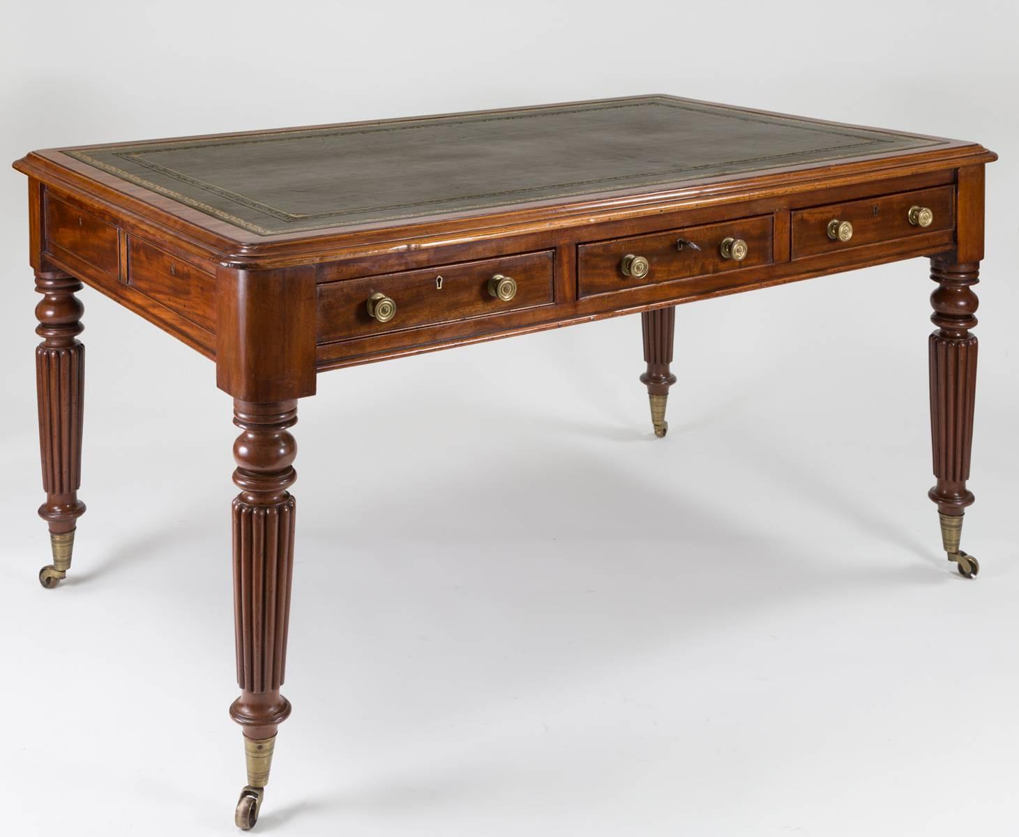 Regency mahogany partners writing table with molded top edge and having six cock beaded drawers with brass knobs, the top covered with antiqued green leather with gilt tooling, supported on reeded and turned legs ending in brass casters.