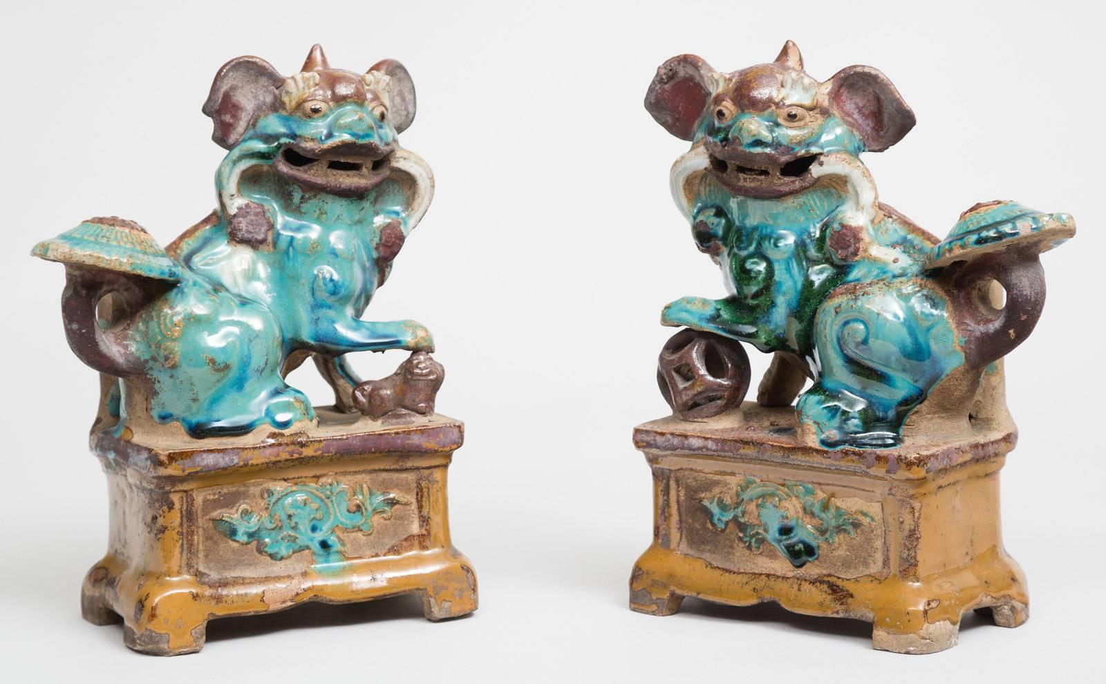 Pair of Chinese green-glazed pottery foo dog incense holders with fierce faces and large ears. The male with fore paw resting on a pierced orb and the females with fore paw resting on her baby. Both raised on rectangular bases.