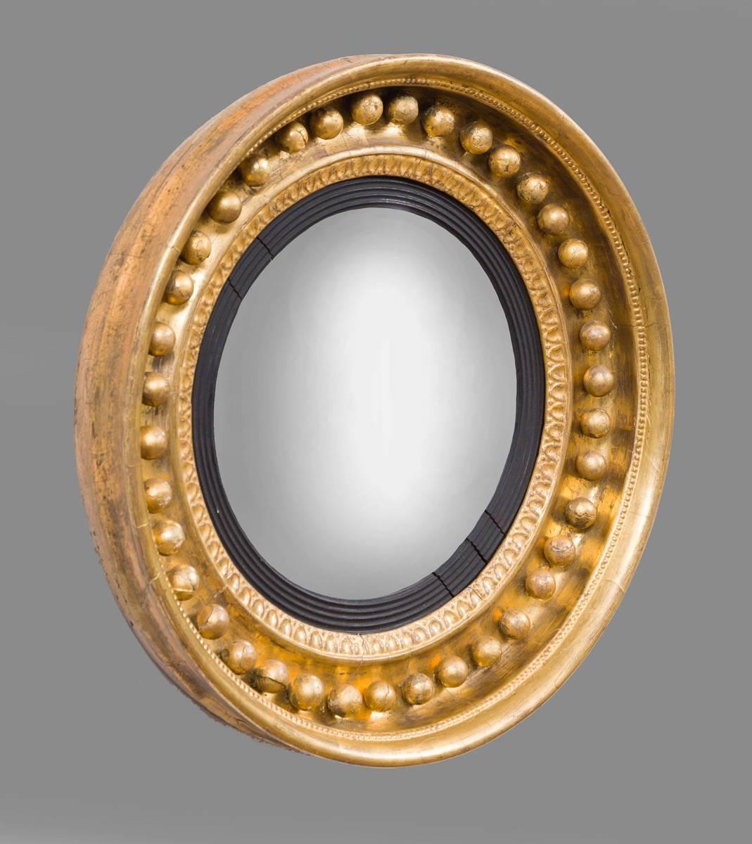 Regency period giltwood convex wall mirror, the circular mirrored plate and reeded slip and egg and dart border set within a deep molded concave frame set with gilded spherules, the outer frame surrounded by a small beaded border.