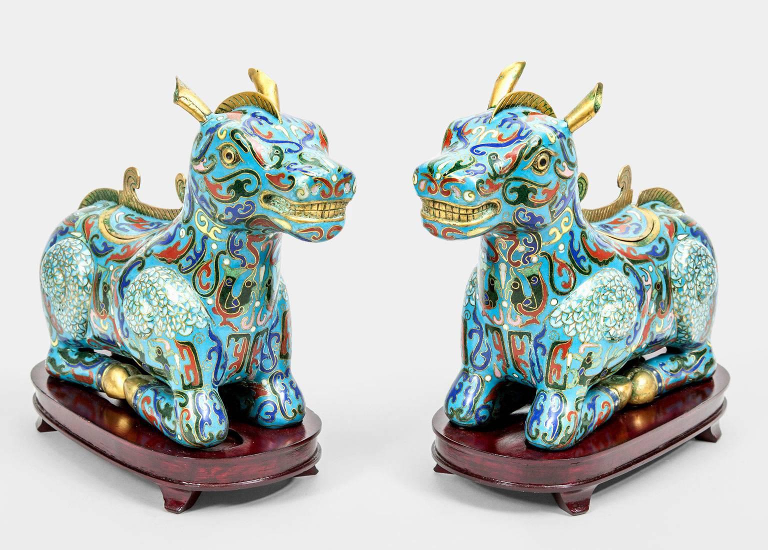 A whimsical pair of antique Chinese cloisonné incense burners in the form of kneeling horses on wooden stands, with removable lids, in enamel colors of turquoise, red, cobalt blue, green, yellows and white with gilded mane, ears, eyes, teeth and