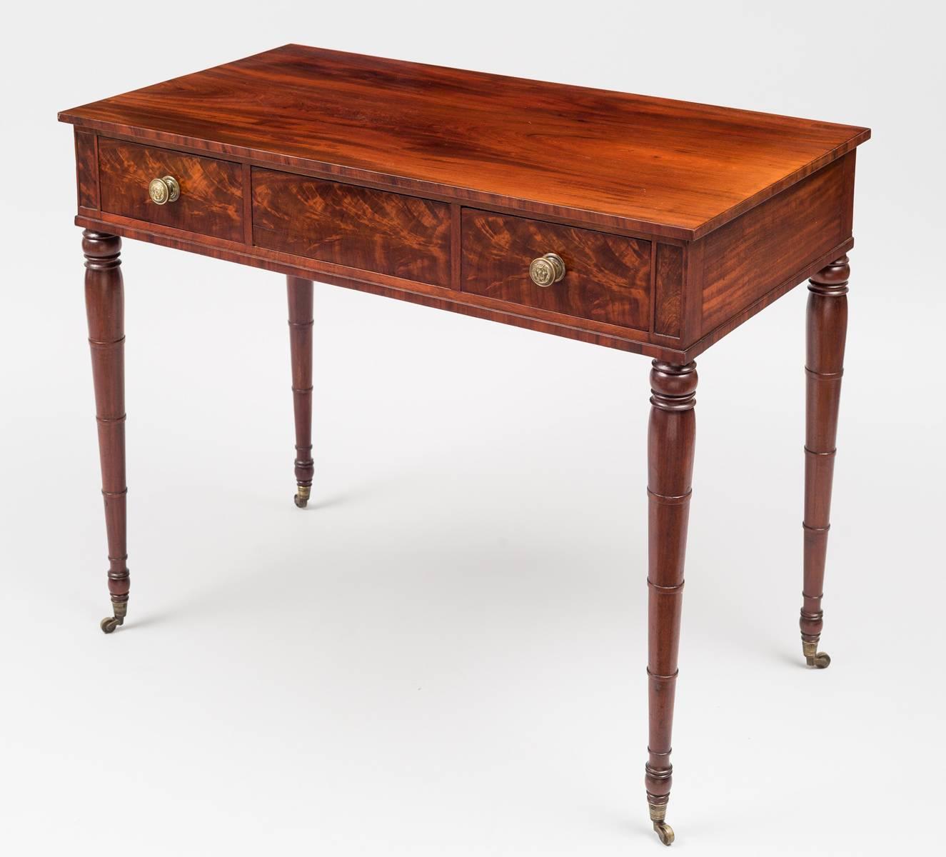 Very fine Sheraton boldly figured mahogany side table with three drawers, centre drawer is blind, original lion’s head brass knobs, Fine ring-turned slender legs on casters. Oak secondary wood. Extremely well-crafted dovetails.