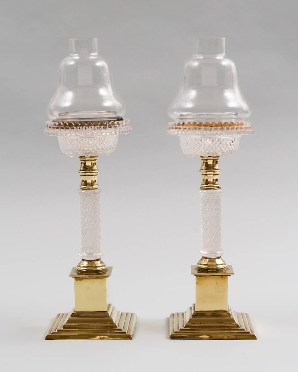 Pair of tall molded glass and brass cricklites. A molded glass circular holder rests atop a brass fitting above a glass column supported by a stepped brass plinth base. Cricklites were slow-burning candle night-lights manufactured by Samuel Clarke