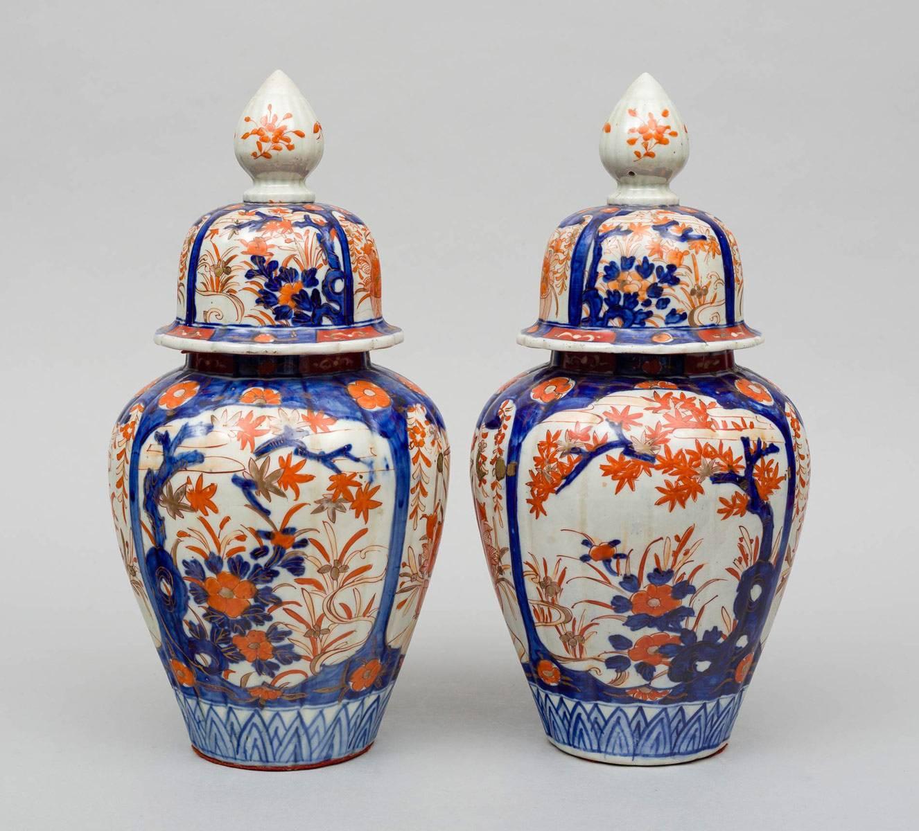 Large pair of Japanese Imari ribbed vases and lids, decorated in iron reds and cobalt blues, the body with four shield-shapes enclosing trees and flowers, the lids with large finials.