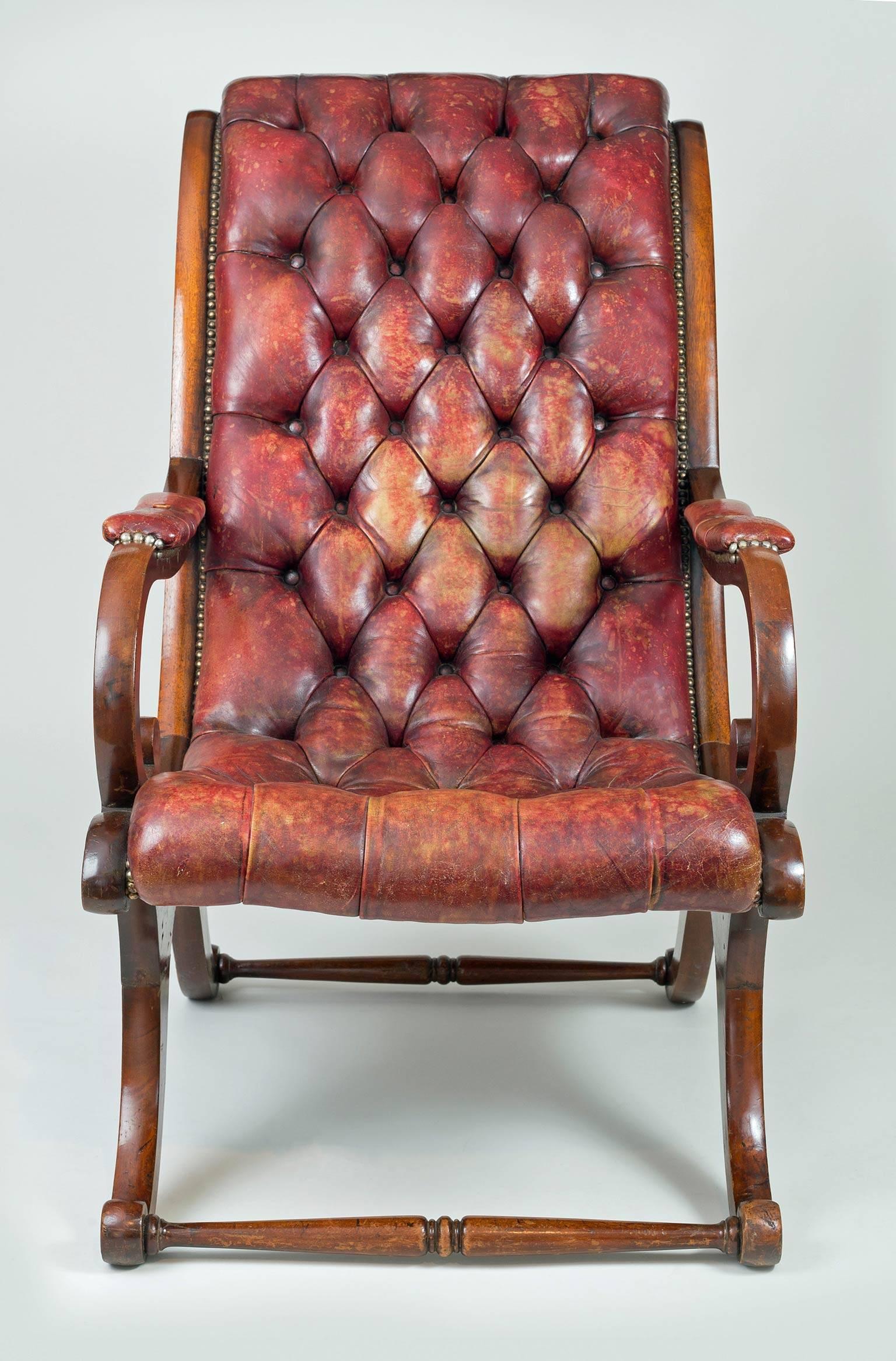 William IV mahogany and leather “sleigh” shaped library armchair with scrolled back, scroll arm supports, C-shaped legs joined by turned stretchers front and back. Upholstered in deep buttoned faded red leather and brass nailheads all around.