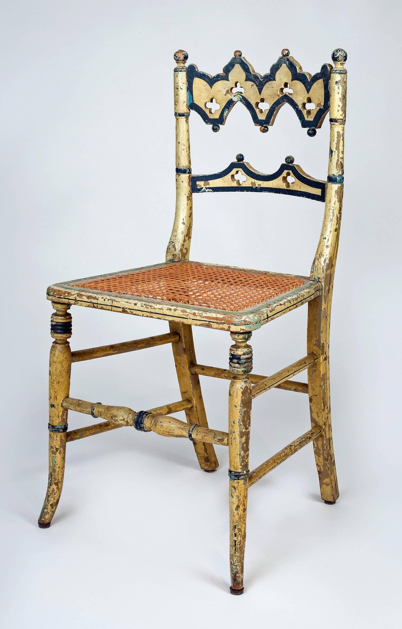 Charming country Gothic Revival side chair with arched back splat with pierced quatrefoil shapes, painted with dark green outlines on a pale yellow background, caned seat, raised on splayed turned legs joined by a turned stretcher in front and five