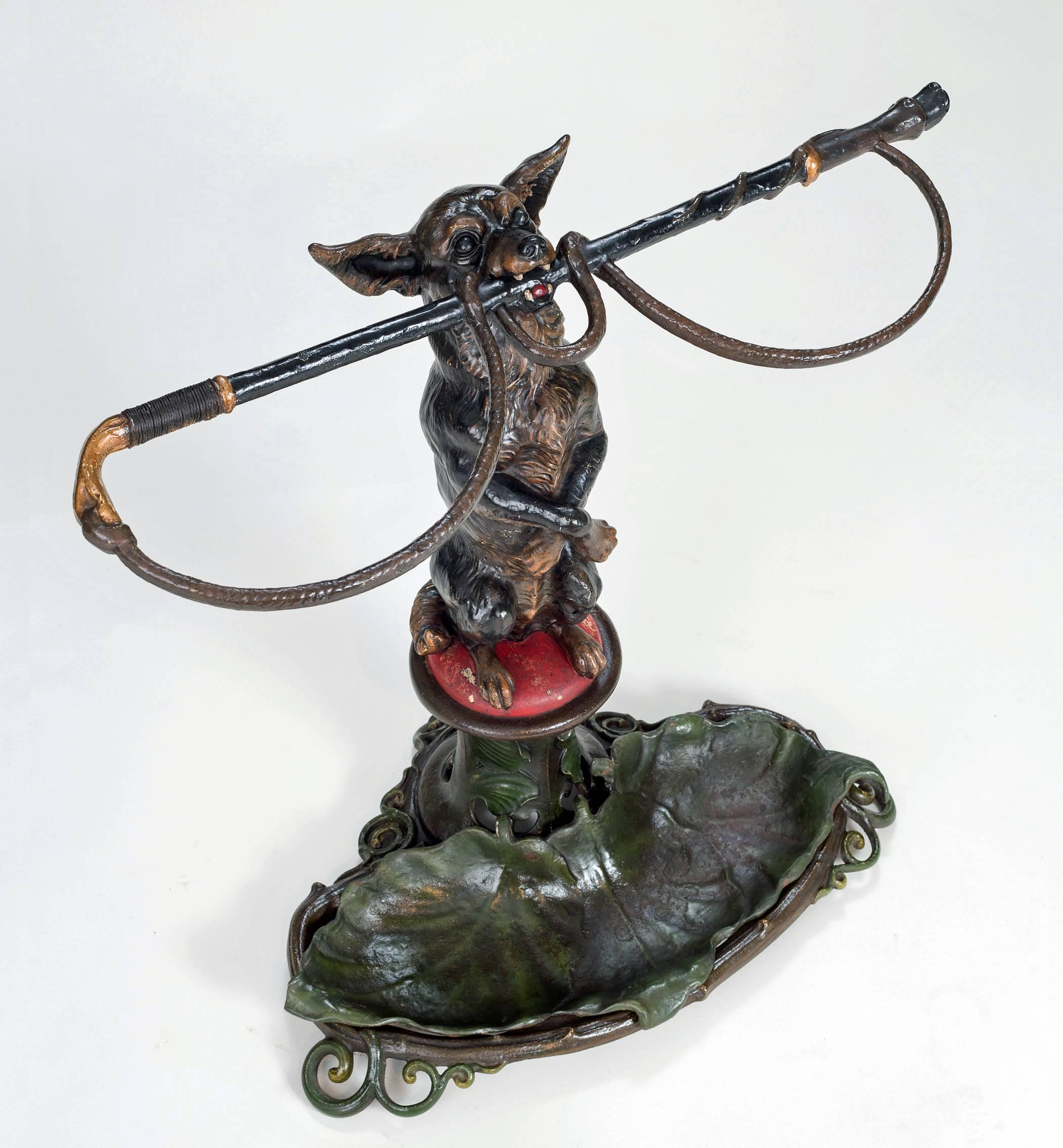 Superb Coalbrookdale cast iron stick or umbrella stand in the form of a chihuahua with a riding crop in its mouth sitting on hind legs on a red cushion with front legs crossed. The removable green drip tray is in the shape of lily pads, the reverse