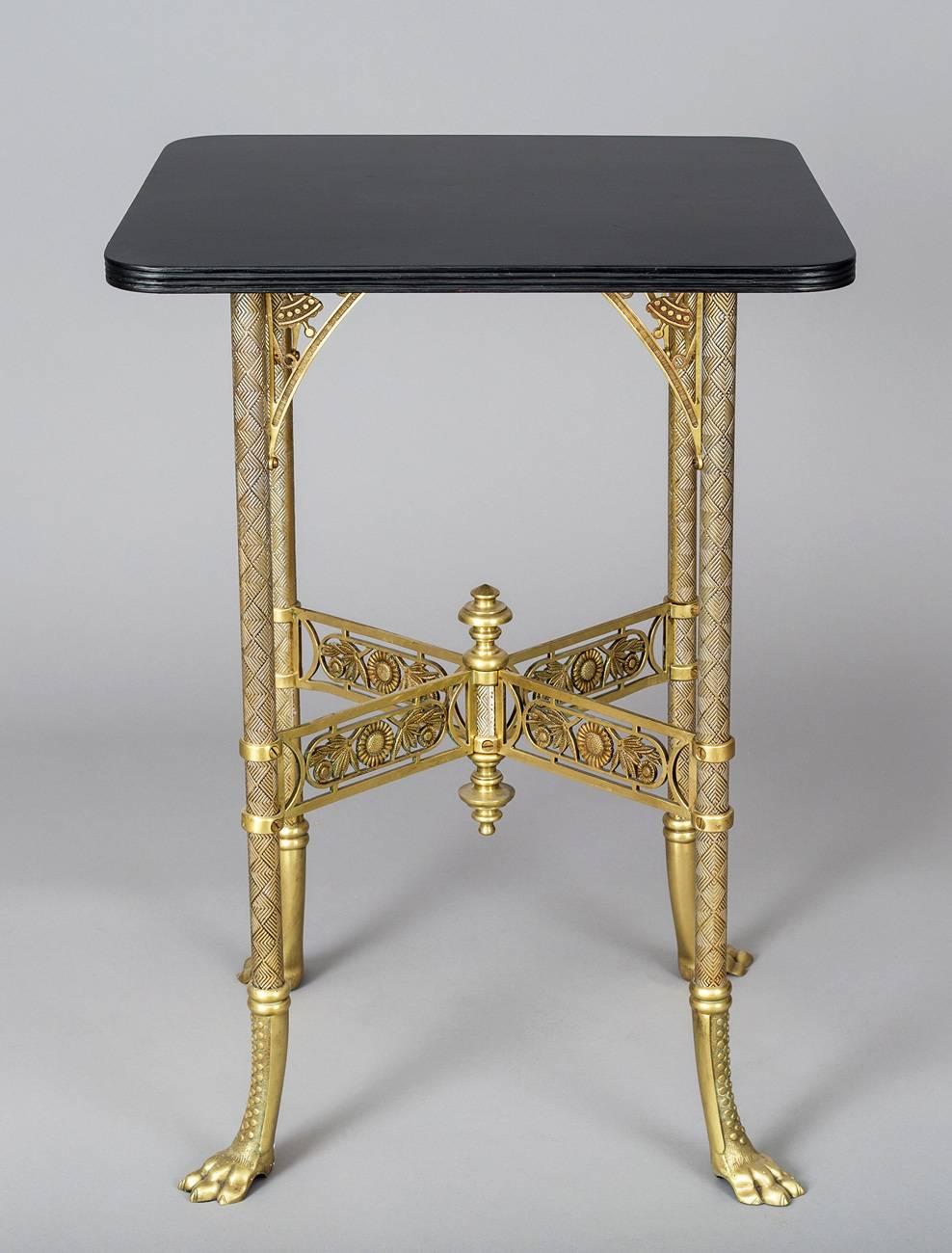 American Aesthetic Movement brass center table with lacquered ebonized top surface with reeded edge, supported by four molded brass legs decorated with diamond shapes, joined by X-shaped pierced stretchers with sunflower motif, centered by brass