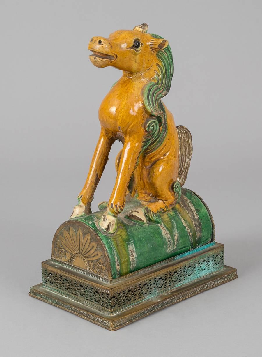 This charming Chinese sancai-glazed pottery roof tile is in the shape of a horse sitting on its haunches with straight front legs, the body is glazed in deep amber, the long mane and details in the hooves are in a green glaze. The whole sits on a